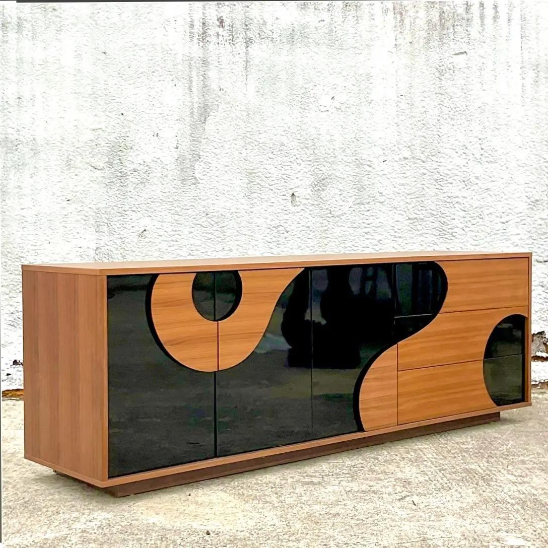 A fantastic vintage contemporary walnut credenza. A chic biomorphic design with a rolling glossy black design. A sleek cabinet with no beautiful wood grain detail. Acquired from a Palm Beach estate.
