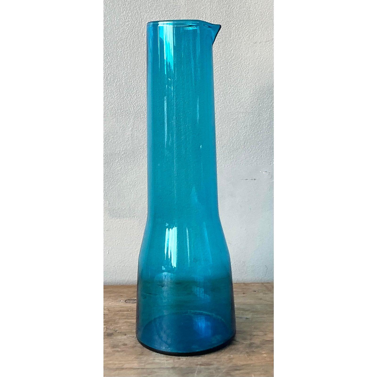 Presenting a striking vintage contemporary teal blue glass beaker pitcher, a piece that effortlessly blends artistic design with functional elegance. This captivating pitcher features a sleek, tall silhouette reminiscent of a laboratory beaker,