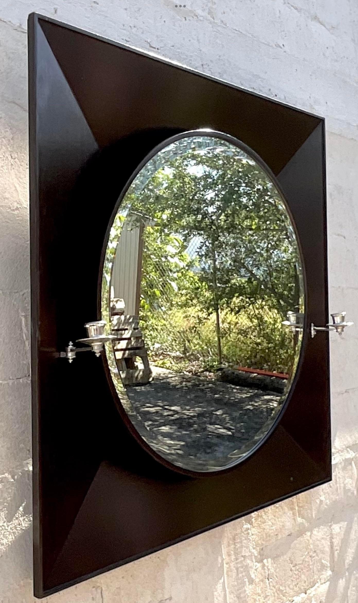 A fabulous vintage contemporary wall mirror. A chic ebony angled frame with two attached candlesticks. The height of chic. Acquired from a Palm Beach estate.