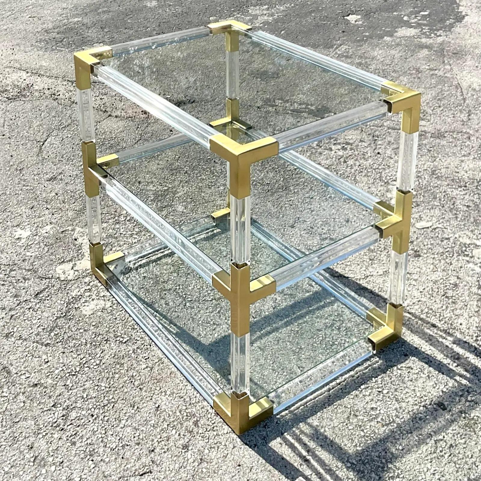 A fabulous vintage Contemporary Lucite side table. A beauty from Jonathan Adler named “Jacques” Lucite rods with brushed brass joints and inset glass shelves. Add a flash of glamour to any space. Acquired from a Palm Beach estate.