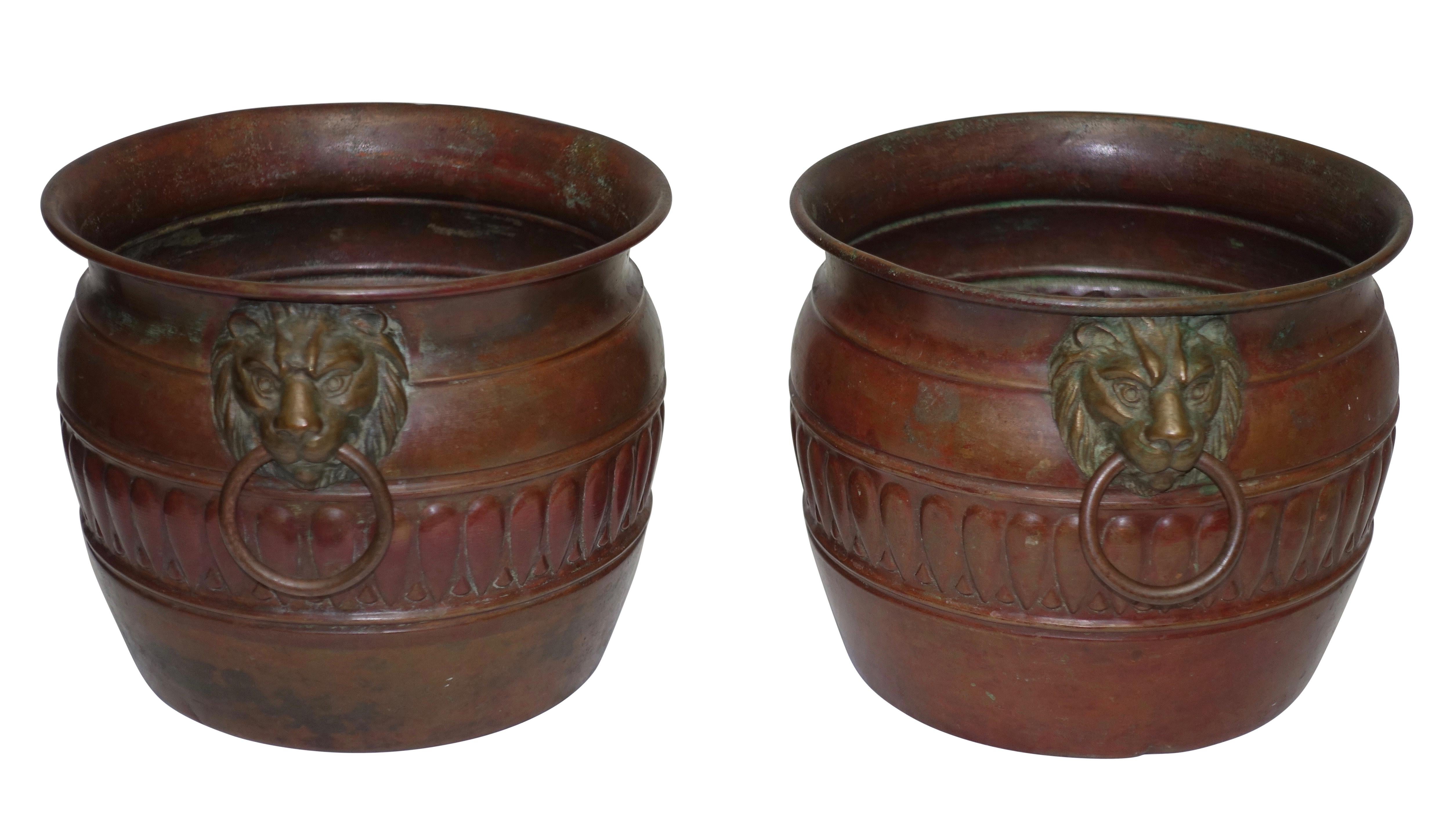 A unique pair of Arts & Crafts style copper cachepots with lion head masks and copper ring handles, pots have a red patinated finish. Both have impressed marks on the underside but are not clear enough to be distinguishable. Italy, mid-20th century.