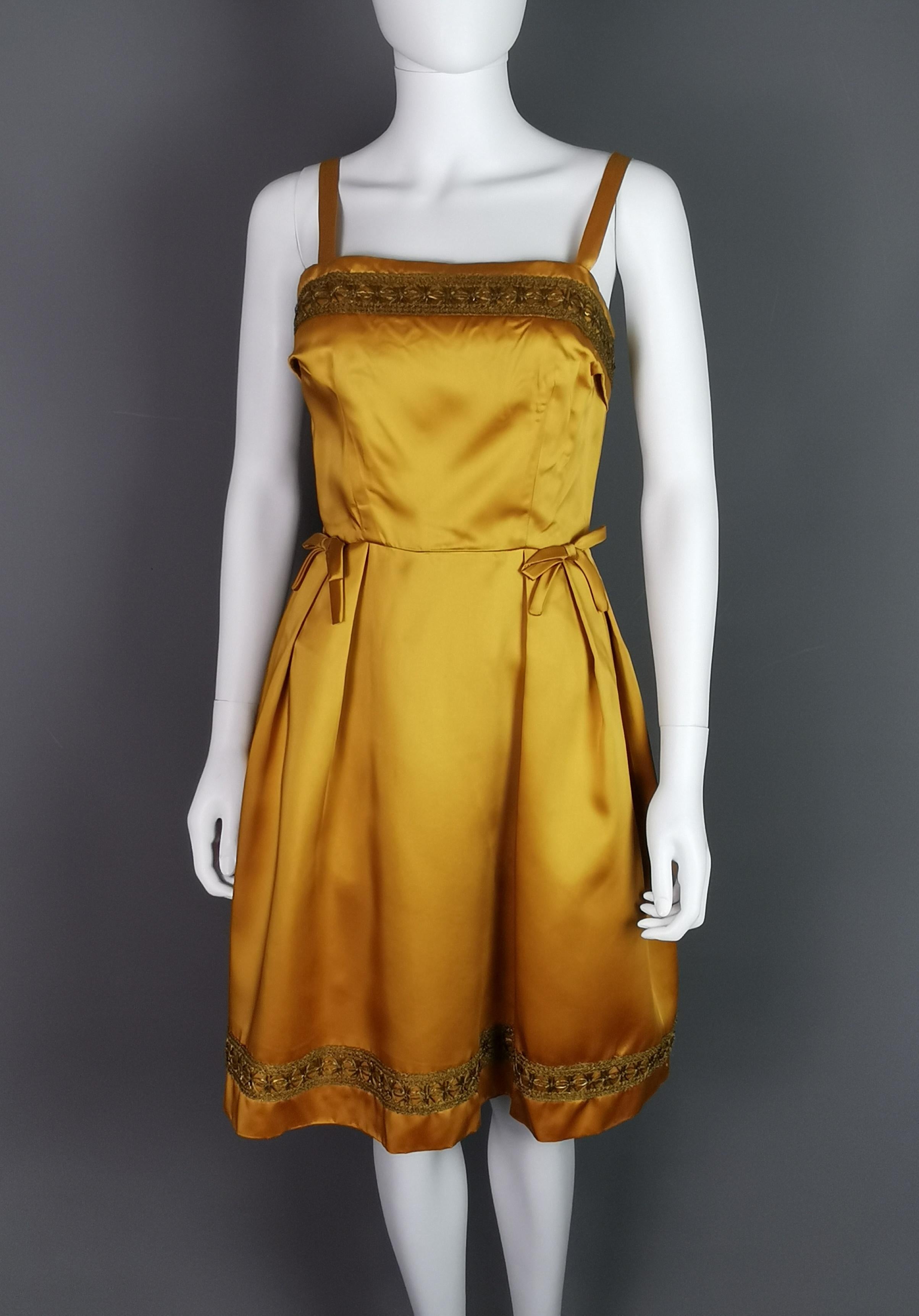 Ein wunderschönes Vintage-Cocktailkleid von Kitty Copeland aus den frühen 1960er Jahren.

Hergestellt aus schwerem kupfer/goldenem Satinstoff und vollständig mit dem Originalfutter gefüttert.

Es ist ein ärmelloses Kleid mit mitteldicken Trägern und