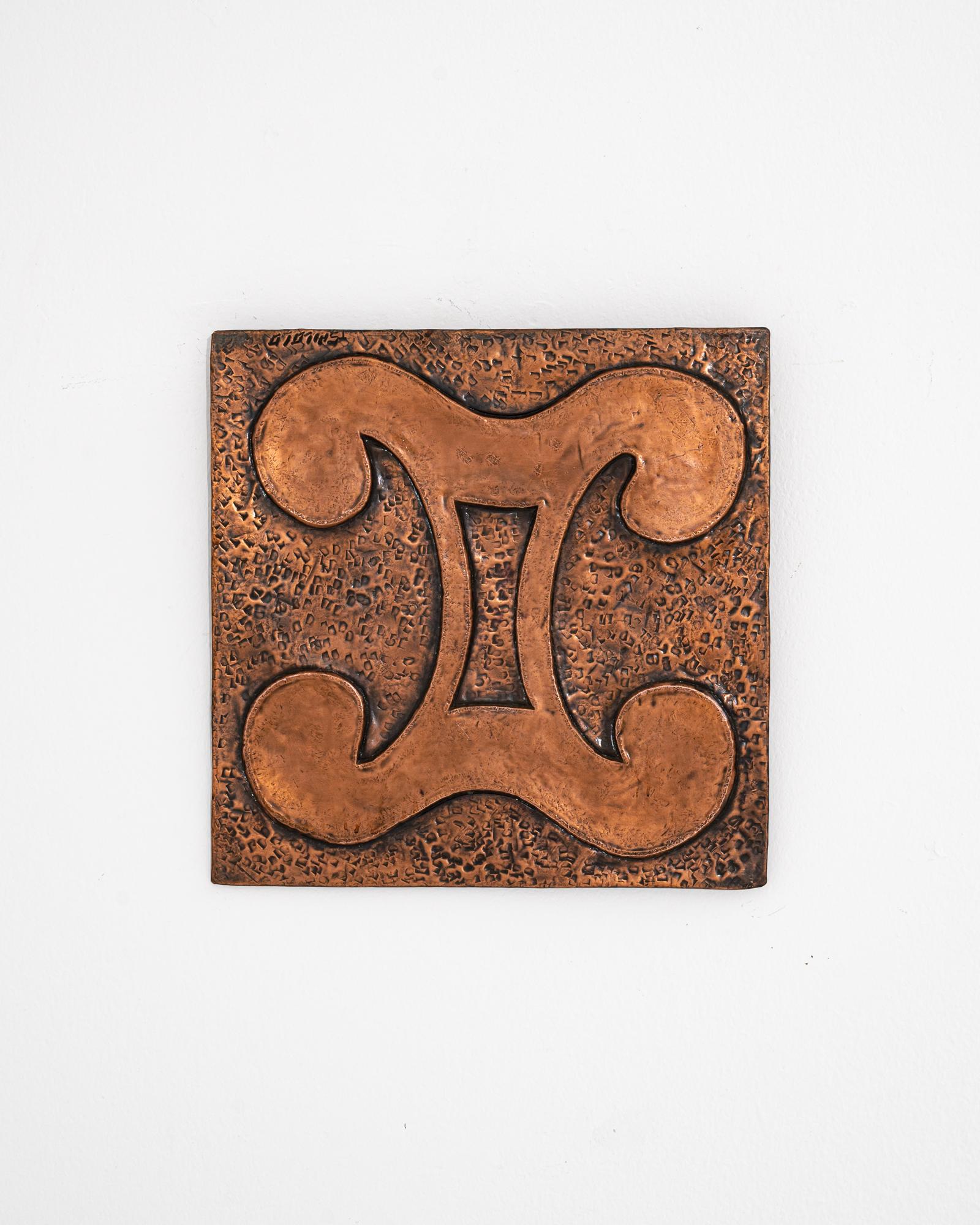 Bold and eye-catching, this copper wall decoration makes a unique vintage accent. The square plaque is decorated with a raised metal symbol —abstract and typographic, the form creates an intriguing motif. The background is composed of marks made by
