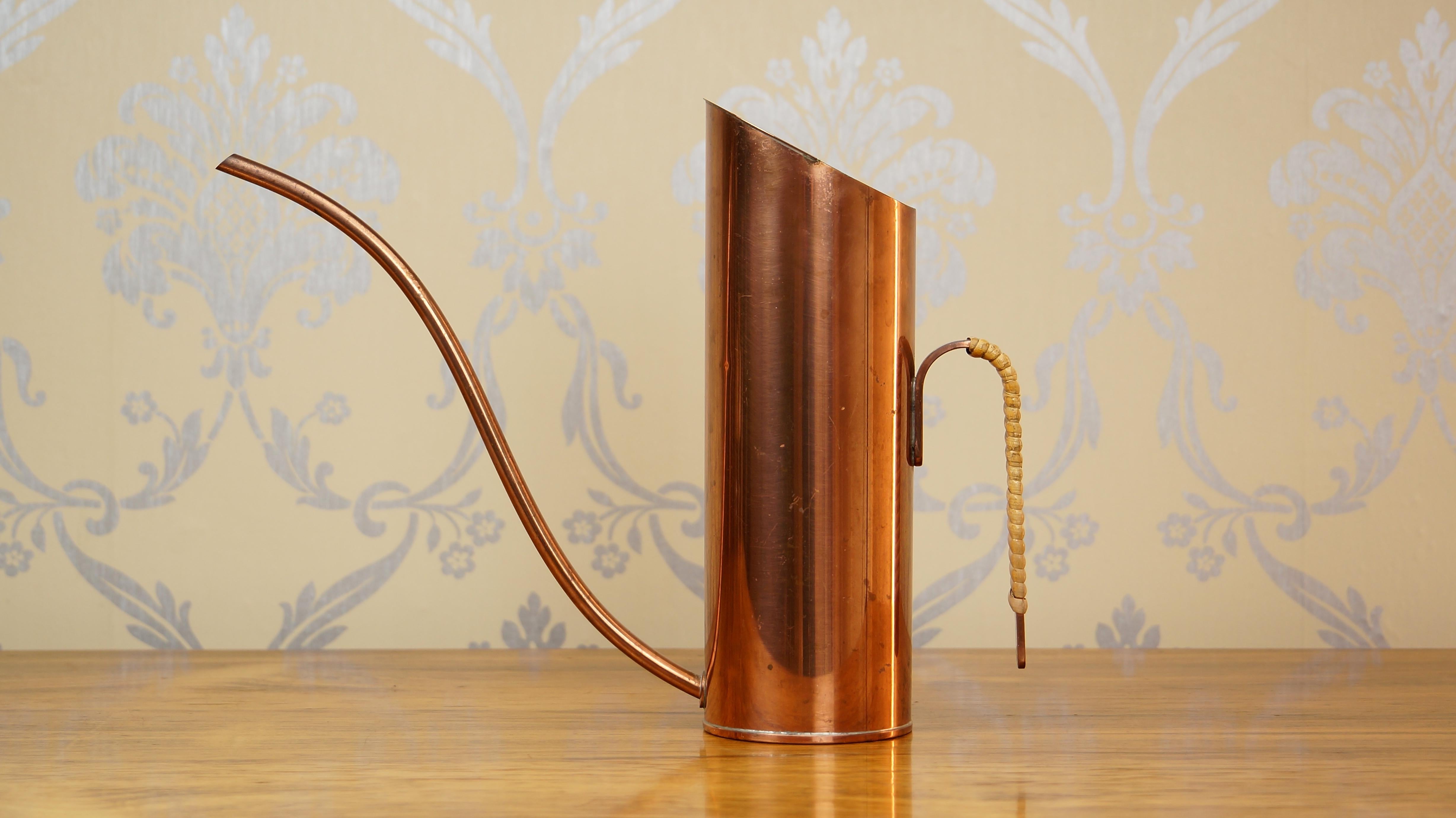An elegant copper watering can or pitcher designed by Gunnar Ander for Ystad Metall, Sweden in the 1950s. 

It features a sculptural spout and striking lines. The beautiful woven rattan handle adds texture to the piece. It is stamped on the