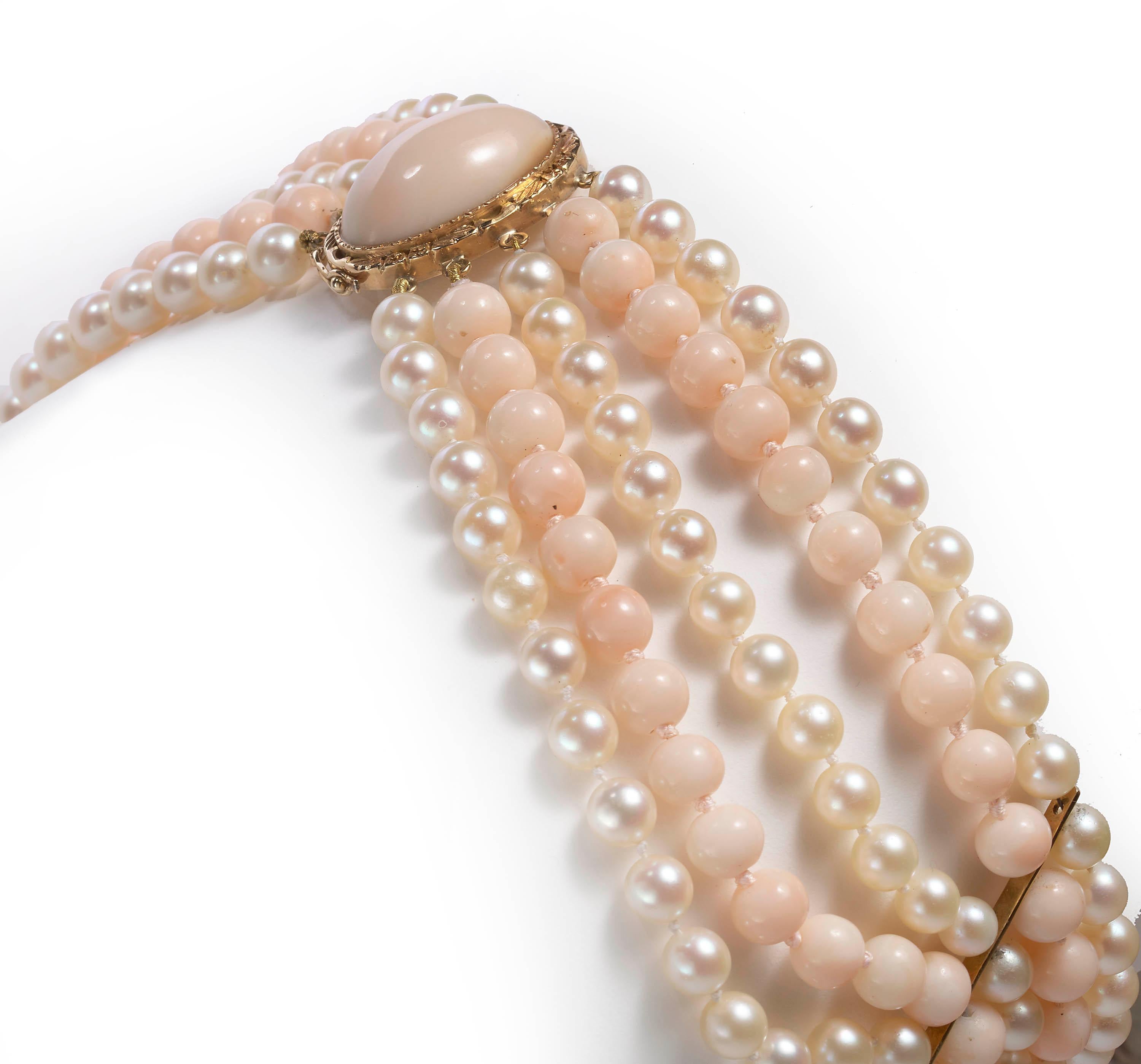 A vintage five row necklace, comprised of three rows of 6mm white cultured pearls and two rows of 8mm round pale pink coral beads, with two 18ct yellow gold spacer bars, strung on to an oval clasp, set with a cabochon coral. Circa 1970. Stamped