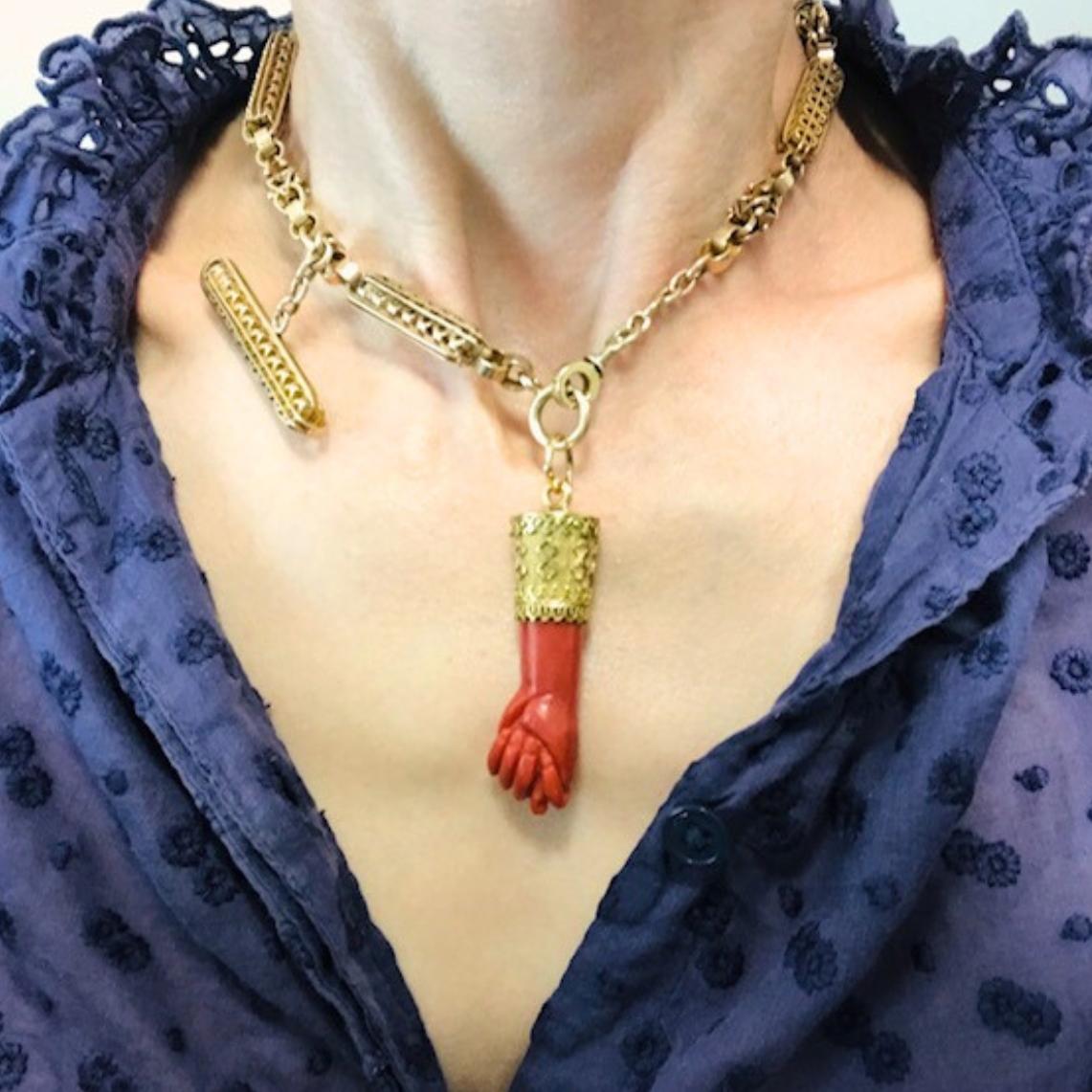 Questa collana vintage combina una catena con alamari in oro 14k con un sorprendente ciondolo a forma di figa in corallo. La catena è disegnata con maglie d'oro allungate e traforate. Ogni maglia ha un dettaglio simile a una filigrana, che