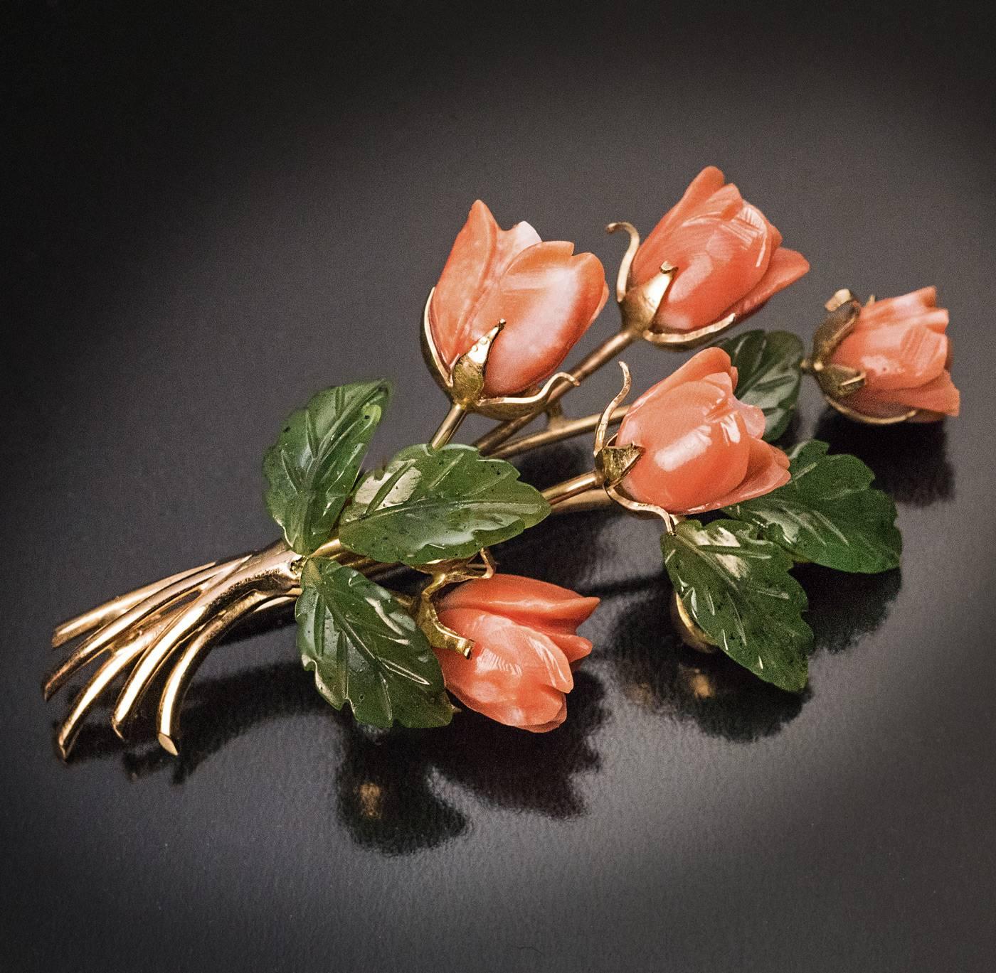 A vintage 14K gold brooch is finely modeled as a spray of roses. The flower heads are naturalistically hand carved from natural salmon pink coral, the leaves – from nephrite jade. 

The brooch was made in Vienna, Austria in the 1950s.

Marked on