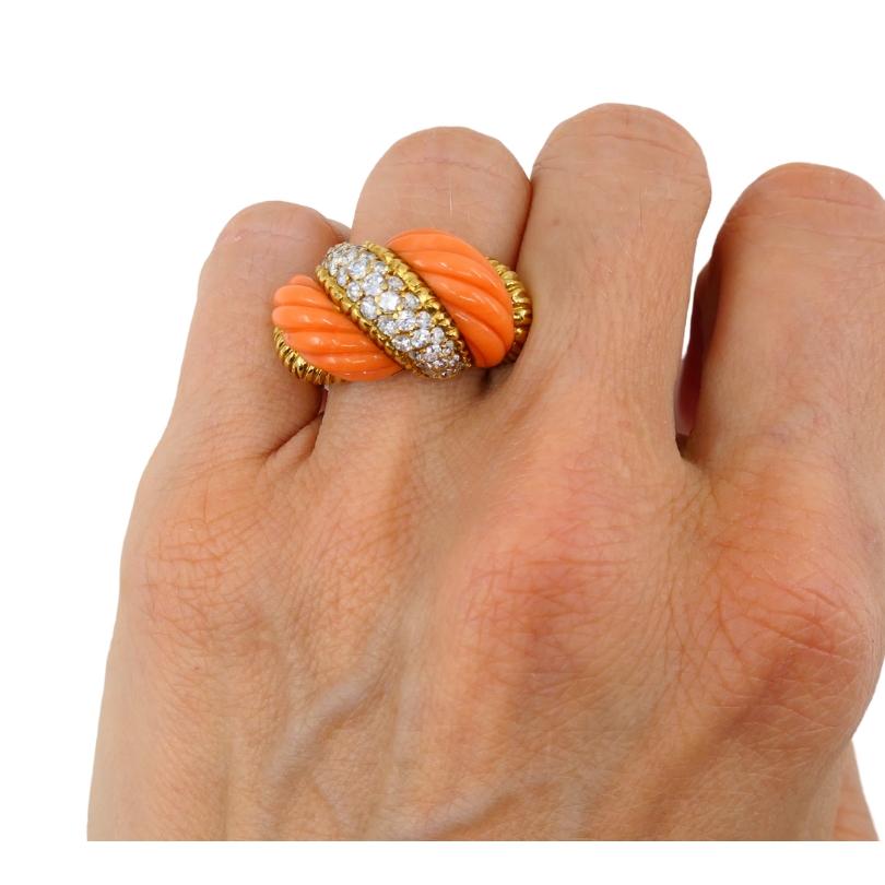Vintage coral ring, crafted of 18k gold, features diamond.
The ring’s centerpiece features two twisted, carved coral sections. A diagonal gold band, encrusted with round cut diamonds, runs across the coral. The gold detailing around the coral and