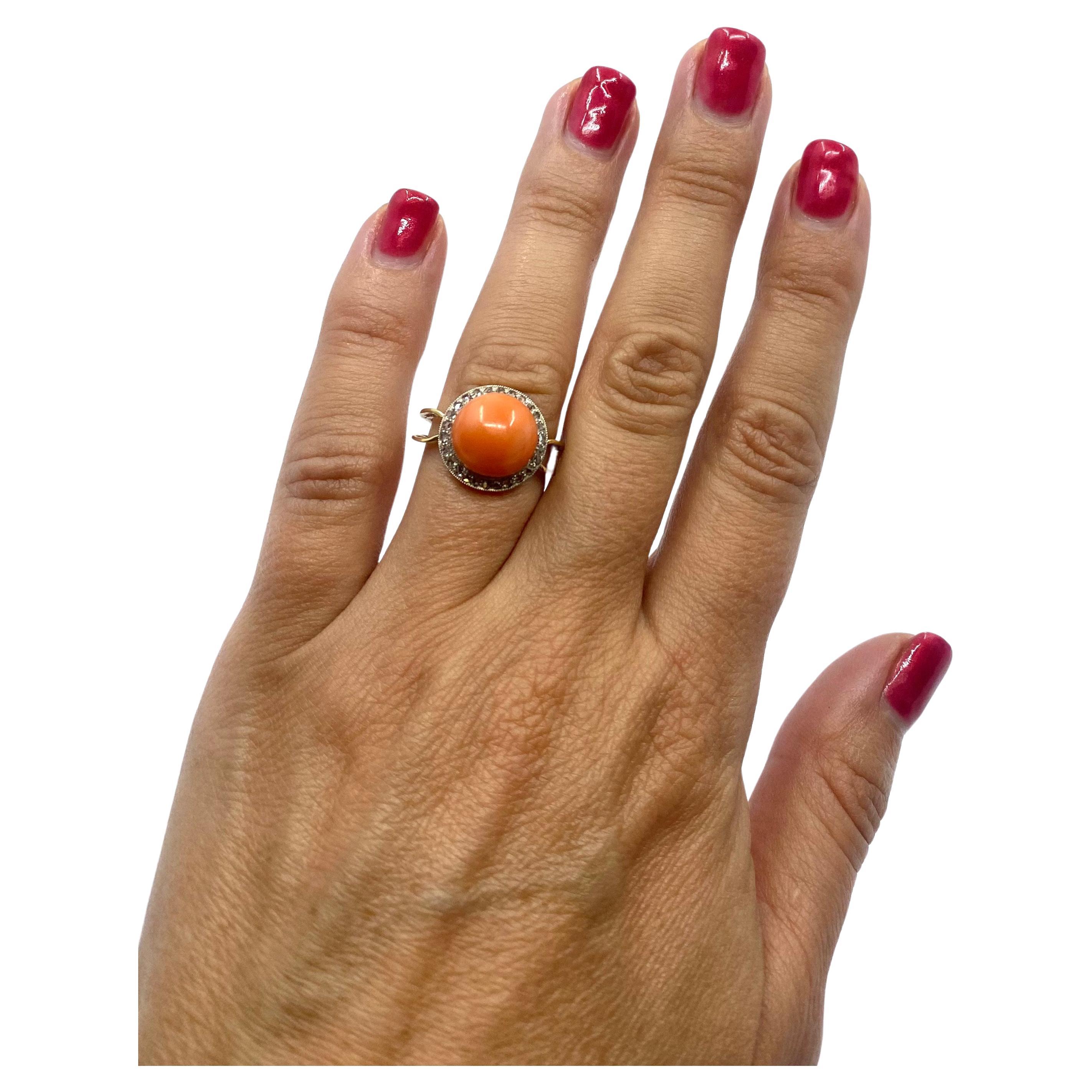 Un precioso anillo vintage de oro de 14 quilates, con coral y diamantes. u2028El coral de un tono rosa salmón se escenifica rodeado de un marco circular de oro blanco adornado con diamantes. La caña está parcialmente calada y se vuelve maciza hacia
