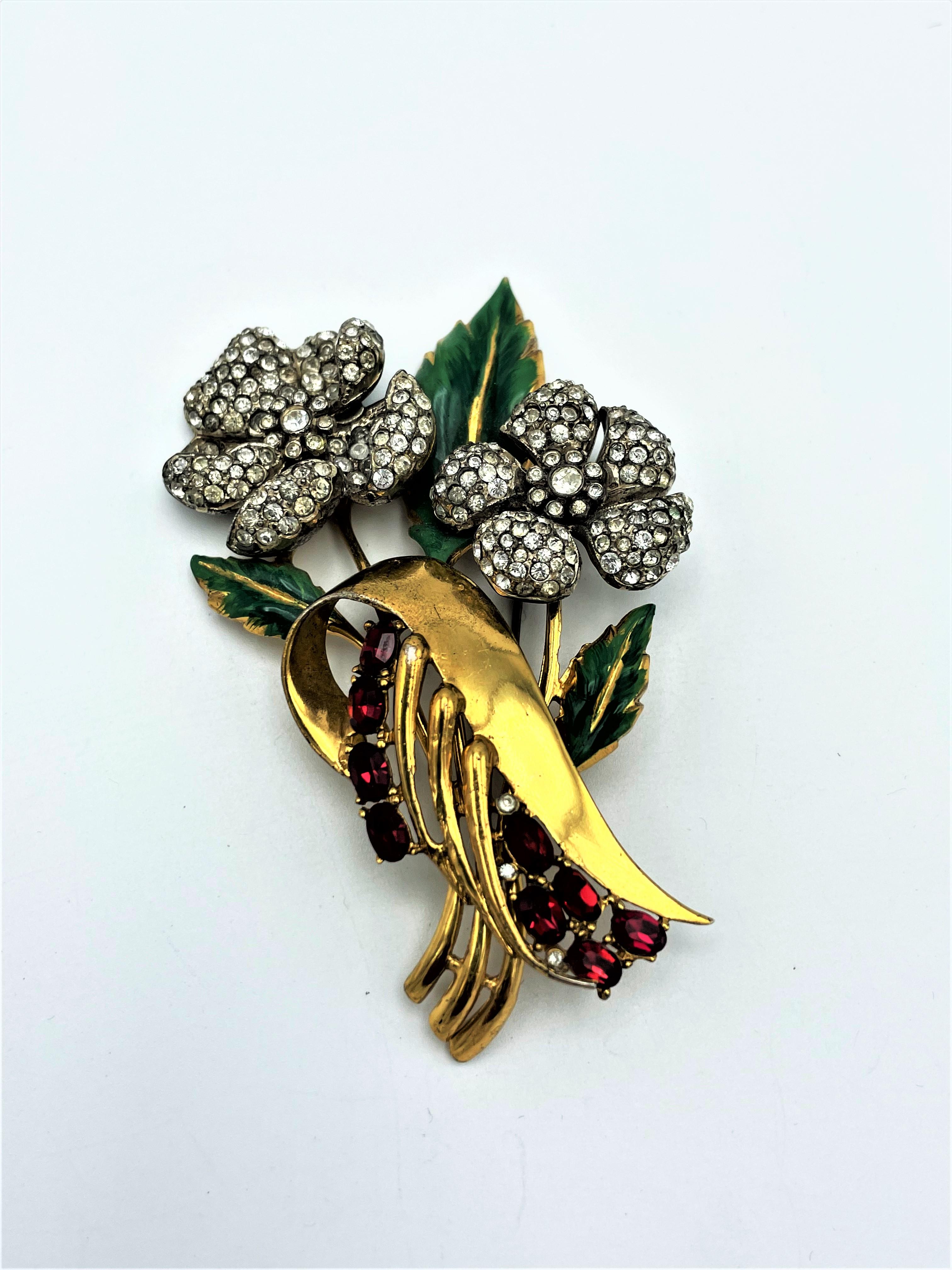 
This beautiful large flower brooch by CoroCraft 1940s USA, with two rhinestone flowers, enameled leaves and red rhinestones. The brooch is made of silver and 24 carat gold plated. Marked  on the back.

Size: H 9 cm x W 6 cm, flower 3 cm x 3 cm. No