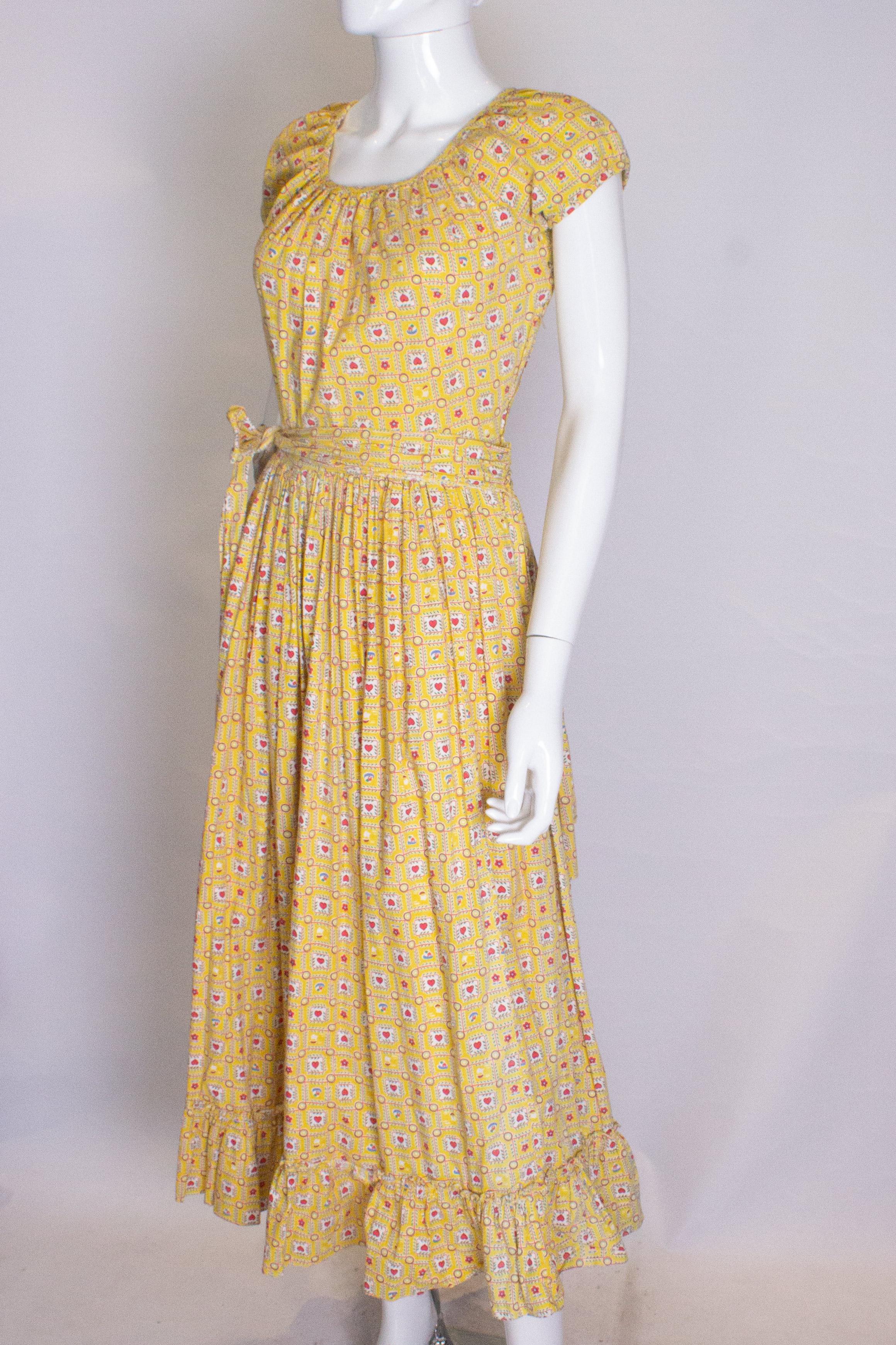 A head turning summer gown from the 1950s, in a wonderful cotton print in yellow, white, red and green. The dress has a wonderful bustle at the back, cap sleaves, a side zip and self fabric belt.