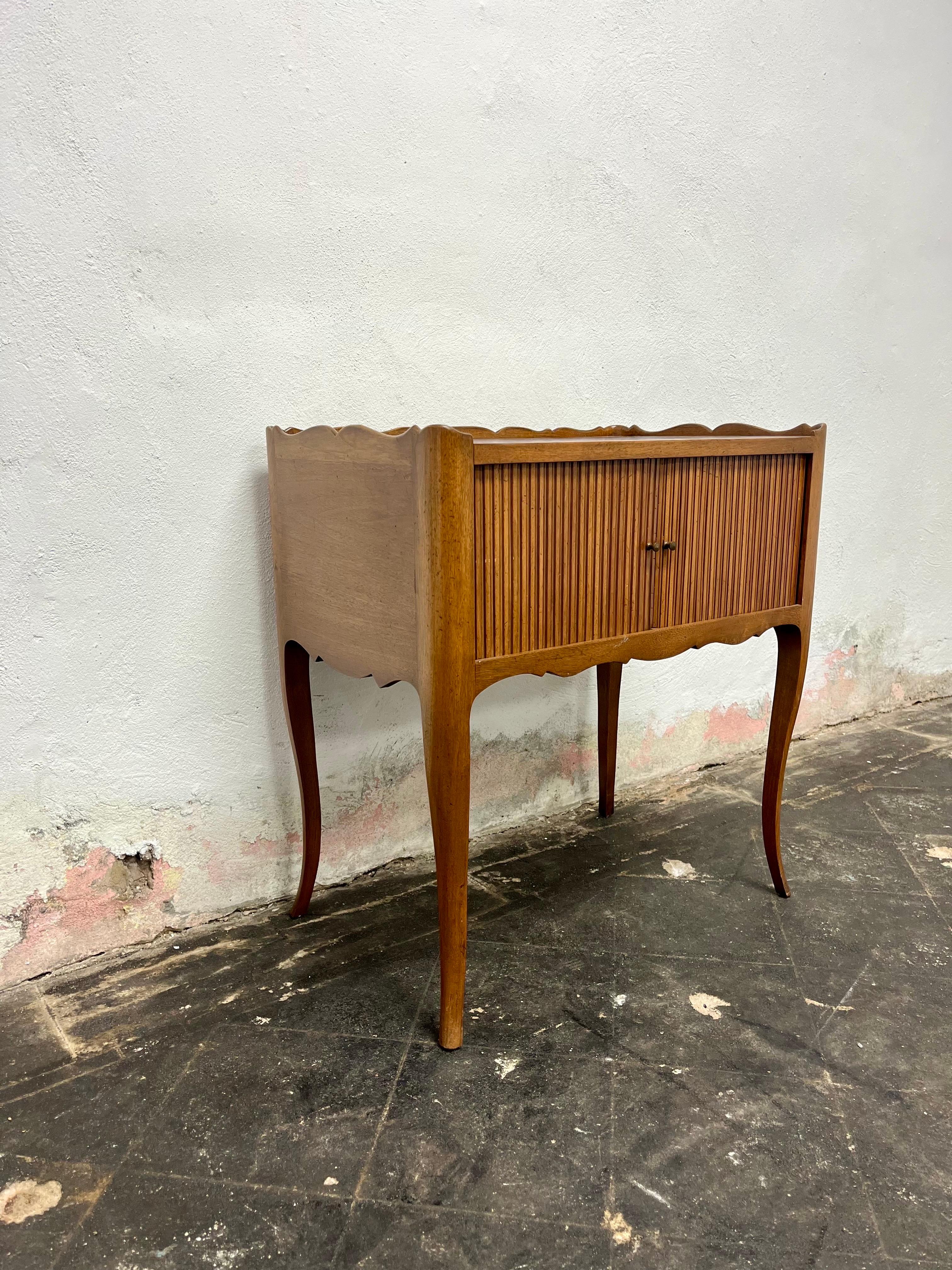 Petite Louis XV style Country French side table or nightstand with tambour doors. Slender curved serpentine legs with scalloped gallery and apron detail. Petite brass handles on easy sliding tambour doors.  A sturdy well-crafted table.
Curbside to