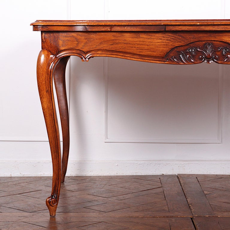 A pretty French Country or Louis XV-style draw-leaf table in oak, the shaped apron with hand-carved details, the parquet top with a pull-out leaf at each end, the whole raised on elegant cabriole legs with scroll feet.