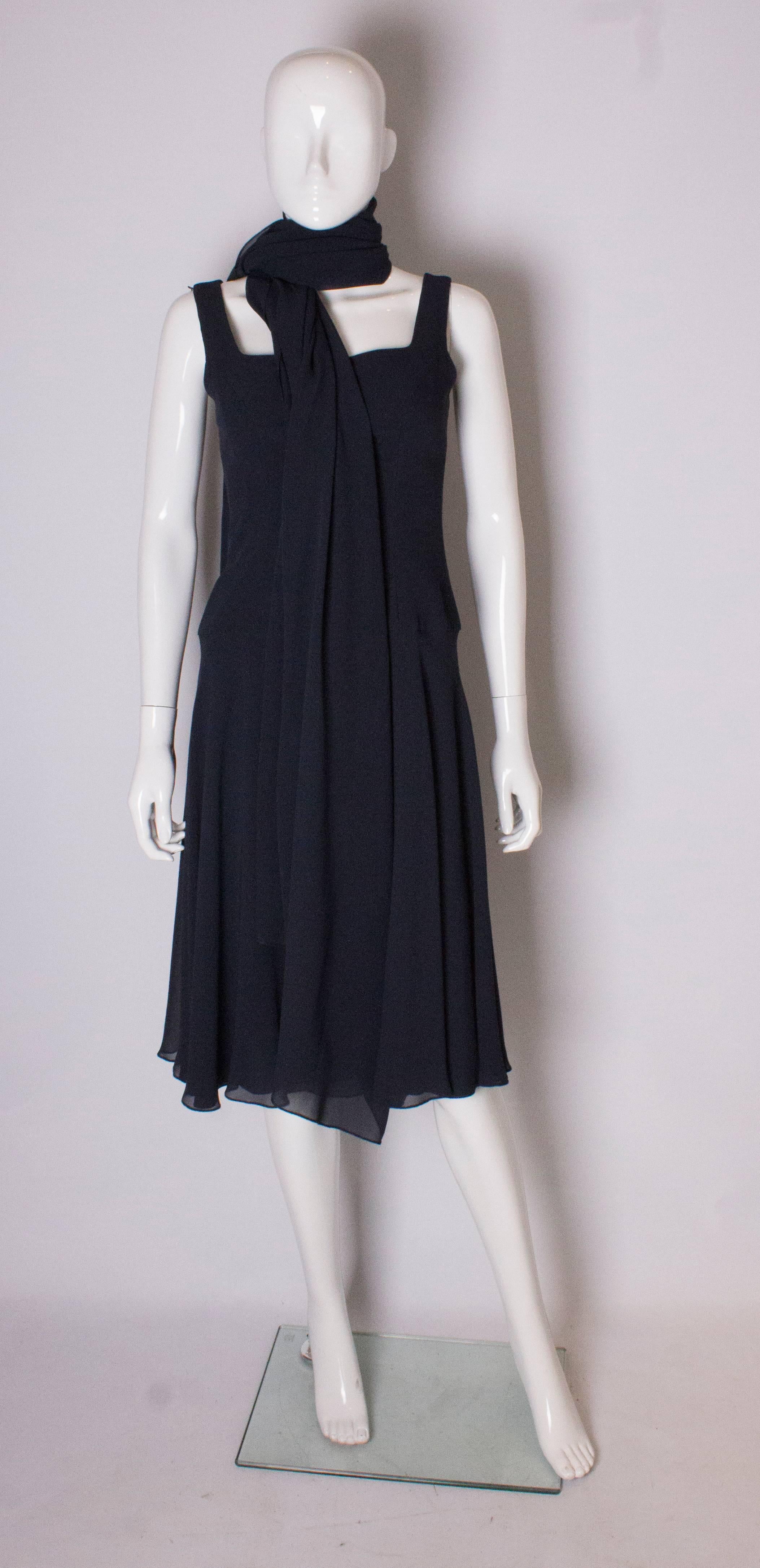 A chic vintage couture silk dress and scarf by Bruce Oldfield .The dress is  in a dark navy blue, and is fitted with a square neckline, sleaveless and lined in silk. It has a flared skirt, and central back zip. The matching silk chiffon scarf