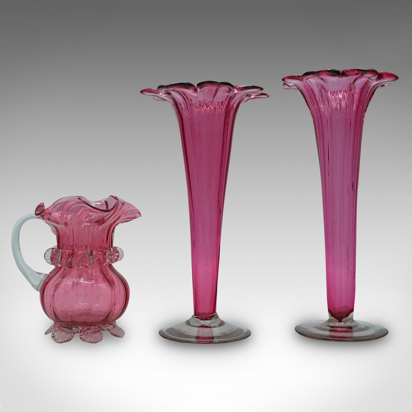 This is a vintage cranberry glass stem vase set. An English, decorative flower slip and replenishment jug, dating to the early 20th century, circa 1930.

Charmingly vibrant glass with delightful fluted forms
Displaying a desirable aged patina and