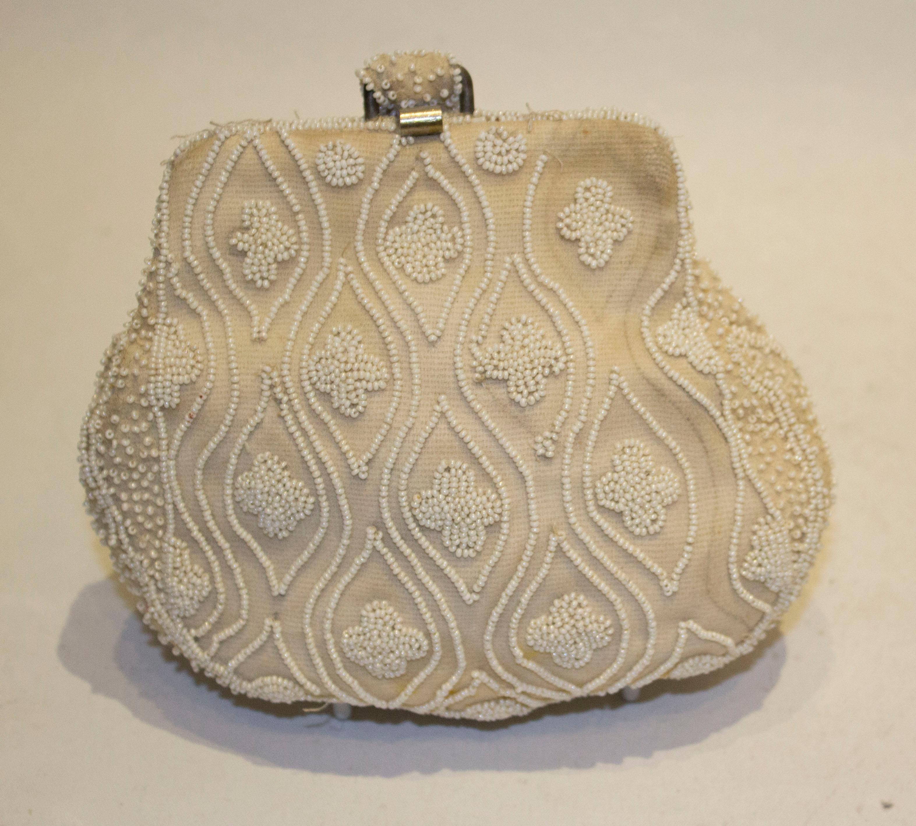 A pretty cream beaded purse in an attractive design. The purse has a central clasp and small handle. Inside there is one pouch pocket. Measurements  width 7'' , height 6''