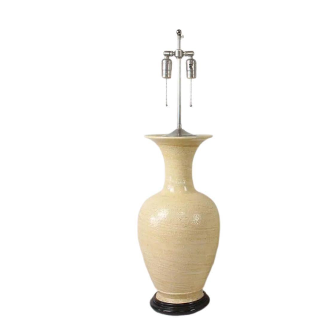 Esta lámpara de sobremesa vintage de cerámica color crema, atribuida al alfarero John Thompson, muestra un distintivo carácter artesanal. La lámpara presenta una forma suavemente redondeada con un cálido esmalte mate en un tono amarillo pálido. El