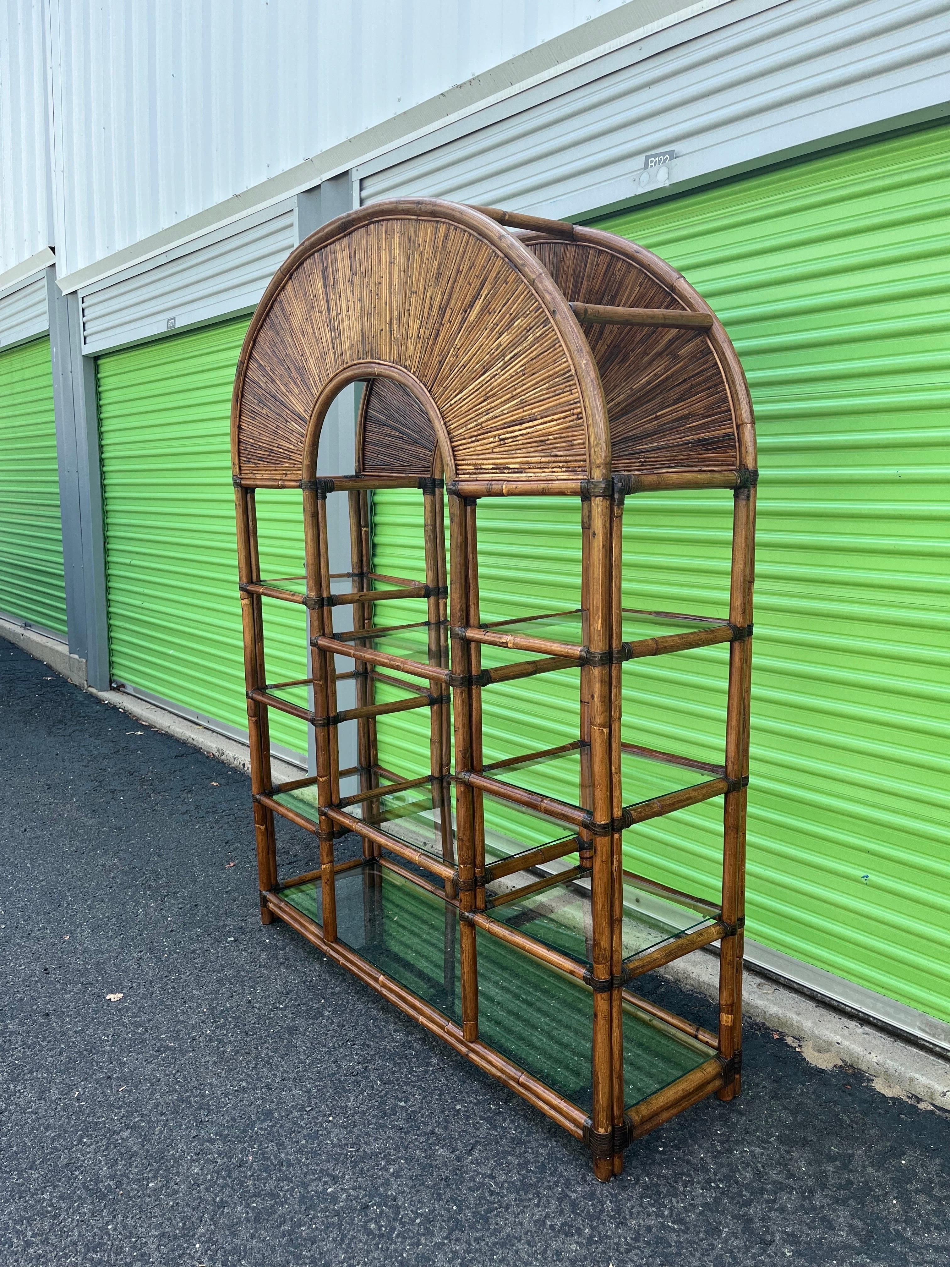 Large rattan etagere features Gabriella Crespi style Rising Sun inlay across arched top and glass shelving for storage and display. Leather wrapped supports. Very good vintage condition with minor imperfections consistent with age. 
Curbside