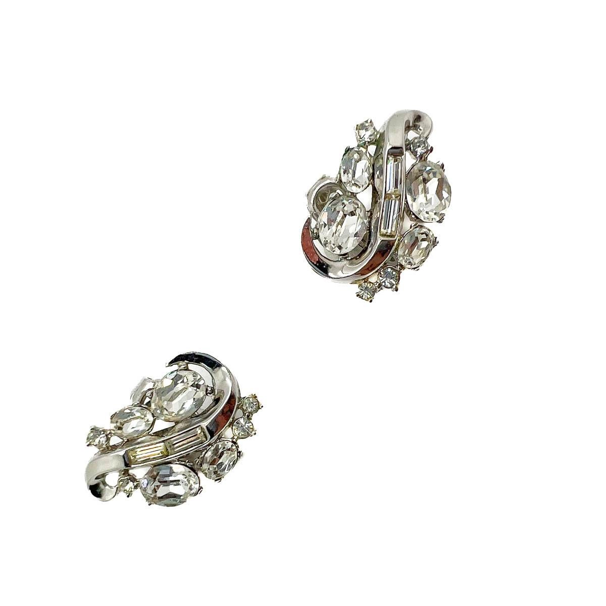 A pair of Vintage Crown Trifari Crystal Swirl Earrings. A stone rich design with large opulent oval crystals accented with rhodium plated detailing set with baguette crystals. A forever classic and totally chic addition to your jewel