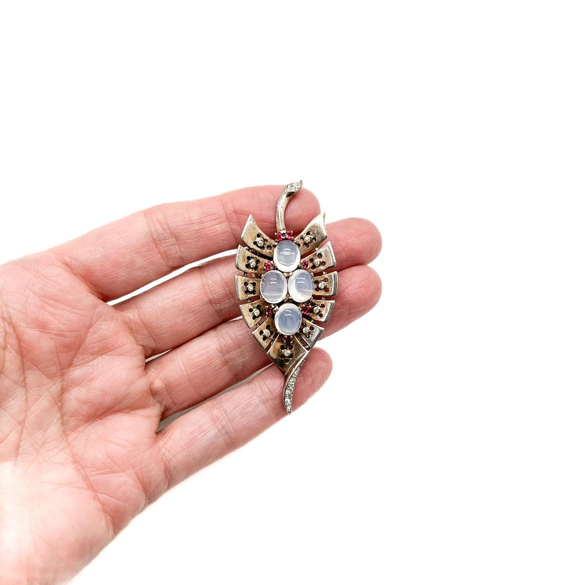 An Art Deco inspired Vintage Crown Trifari Moonstone Leaf Brooch. Featuring a wonderfully crafted solid sterling vermeil silver stylised leaf set with four adorable moonstones and paste chatons in white and contrasting red. An exceptional piece of