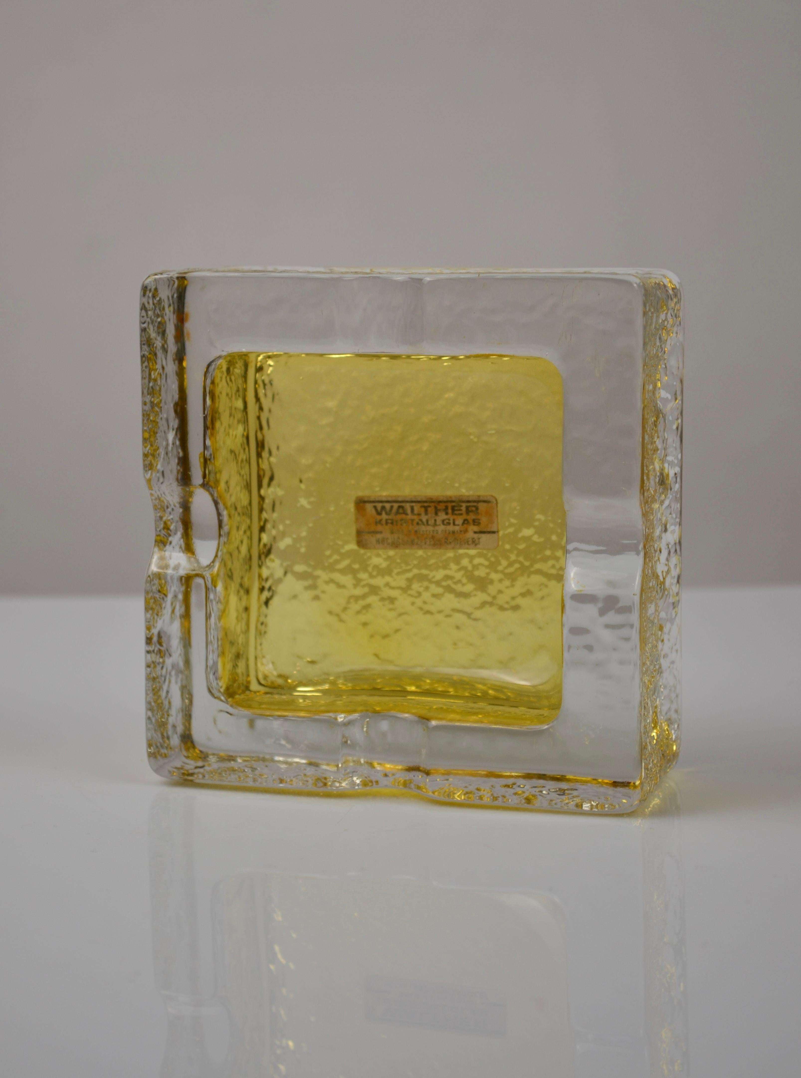 Eleganter Aschenbecher aus der Mitte des Jahrhunderts von Walther Kristallglas, hergestellt in Deutschland, ca. 1970er Jahre.
Dieser quadratische Aschenbecher wirkt durch seine klare Geometrie und das Zusammenspiel zwischen dem klaren, gepressten