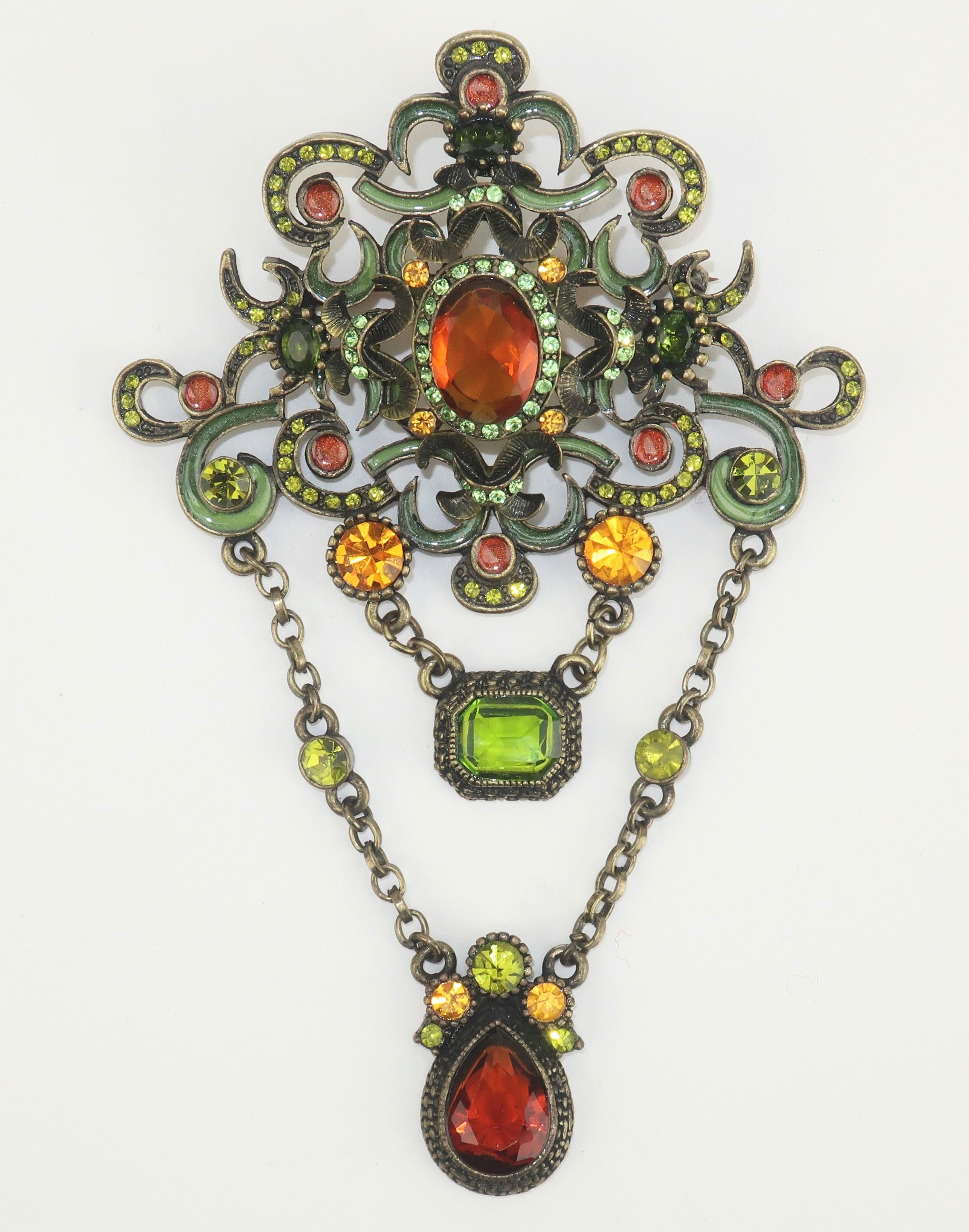 C.1990 brooch with an ornate Old World style reminiscent of Edwardian jewelry.  The bronze tone metal base is embellished with deep green and amber enameling and features two dangling drops accented by green and amber crystal stones.  Outfitted with