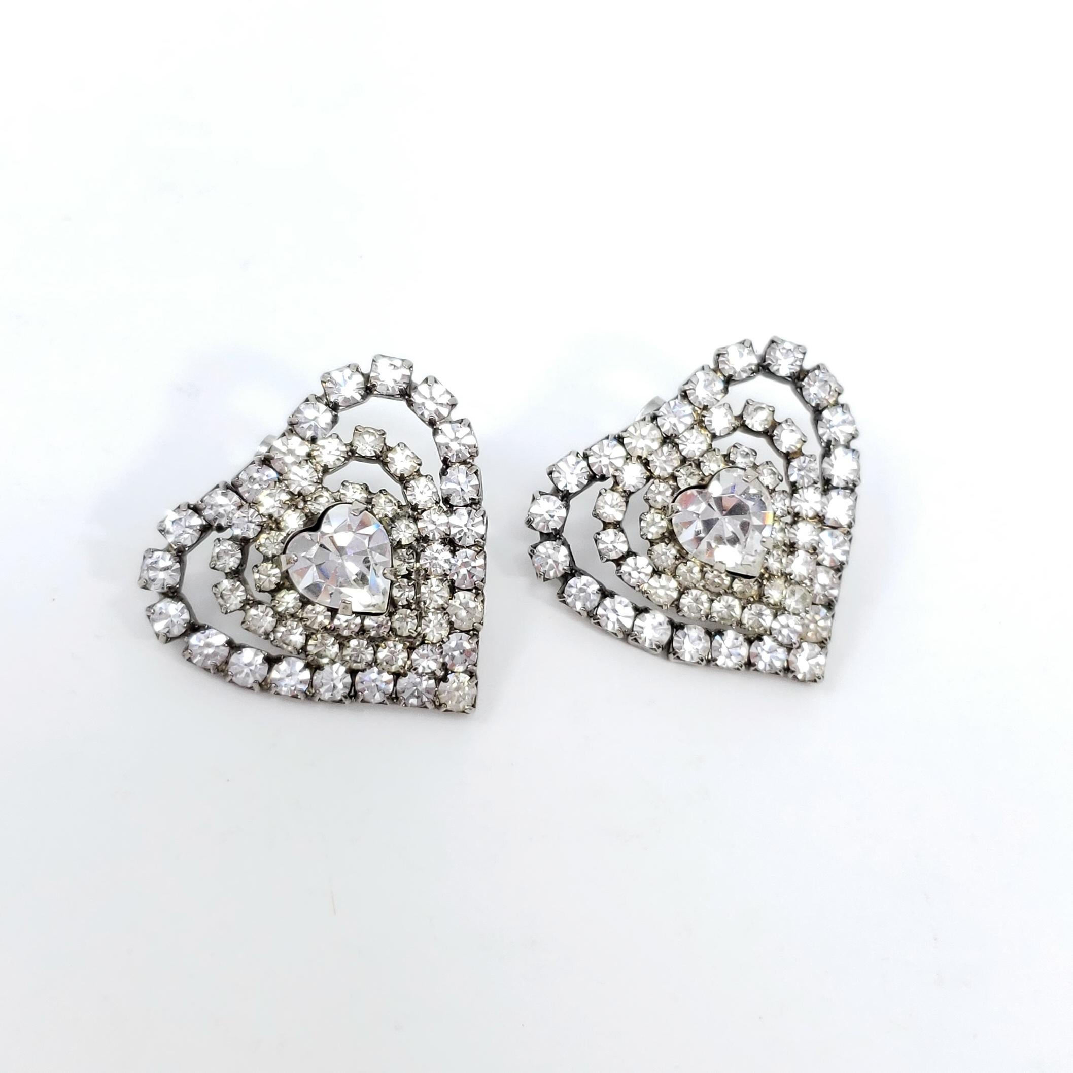 A stylish pair of vintage earrings! These glamorous hearts are decorated with dazzling clear crystals, prong-set in a silver-tone setting.

Post backs. Circa mid 1900s.