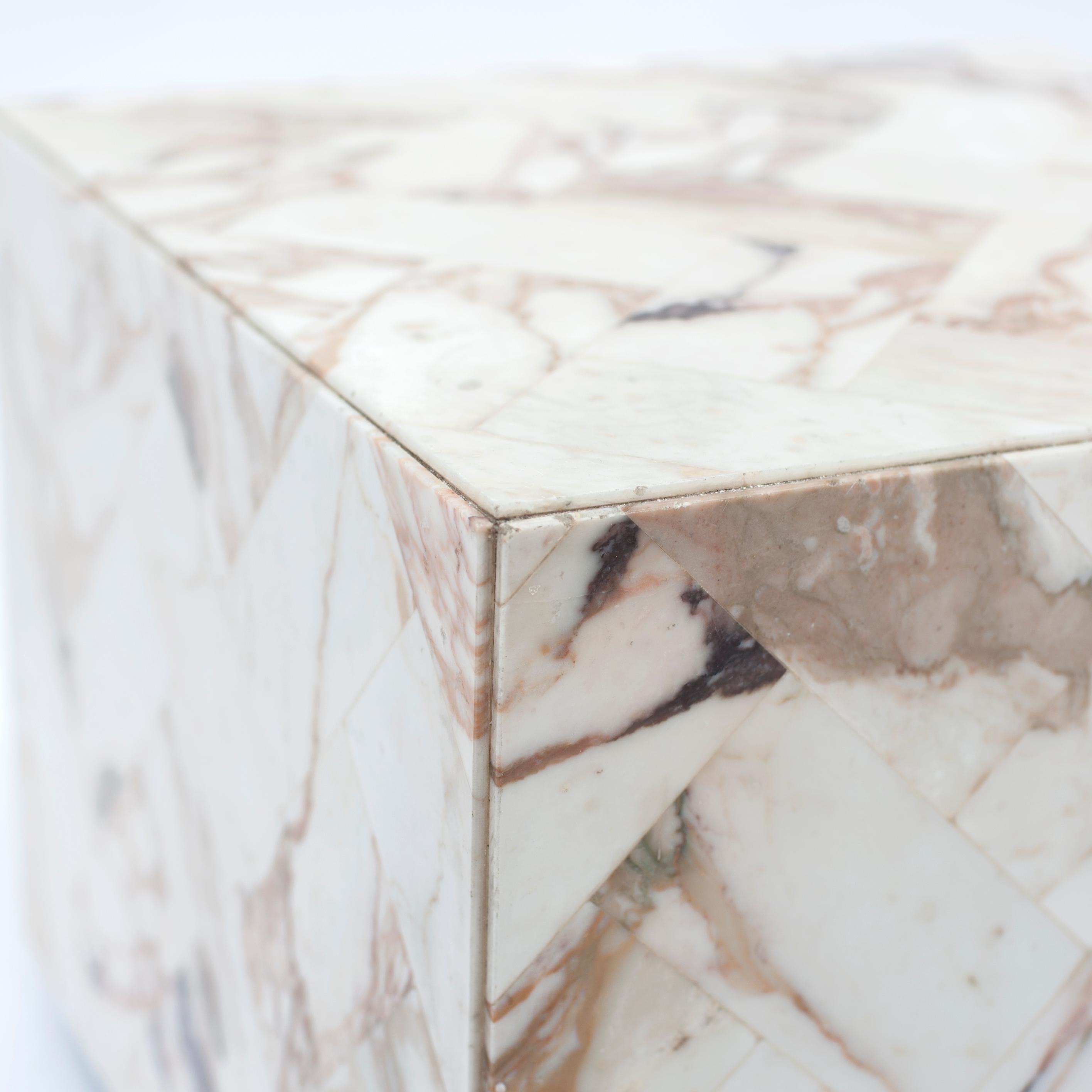 This cube-shaped side table is upholstered with multicolored marble. The table has the shape of a cube and is covered with marble in a herringbone motif on all visible sides. The shape of the table fits very well in a modern interior and forms a