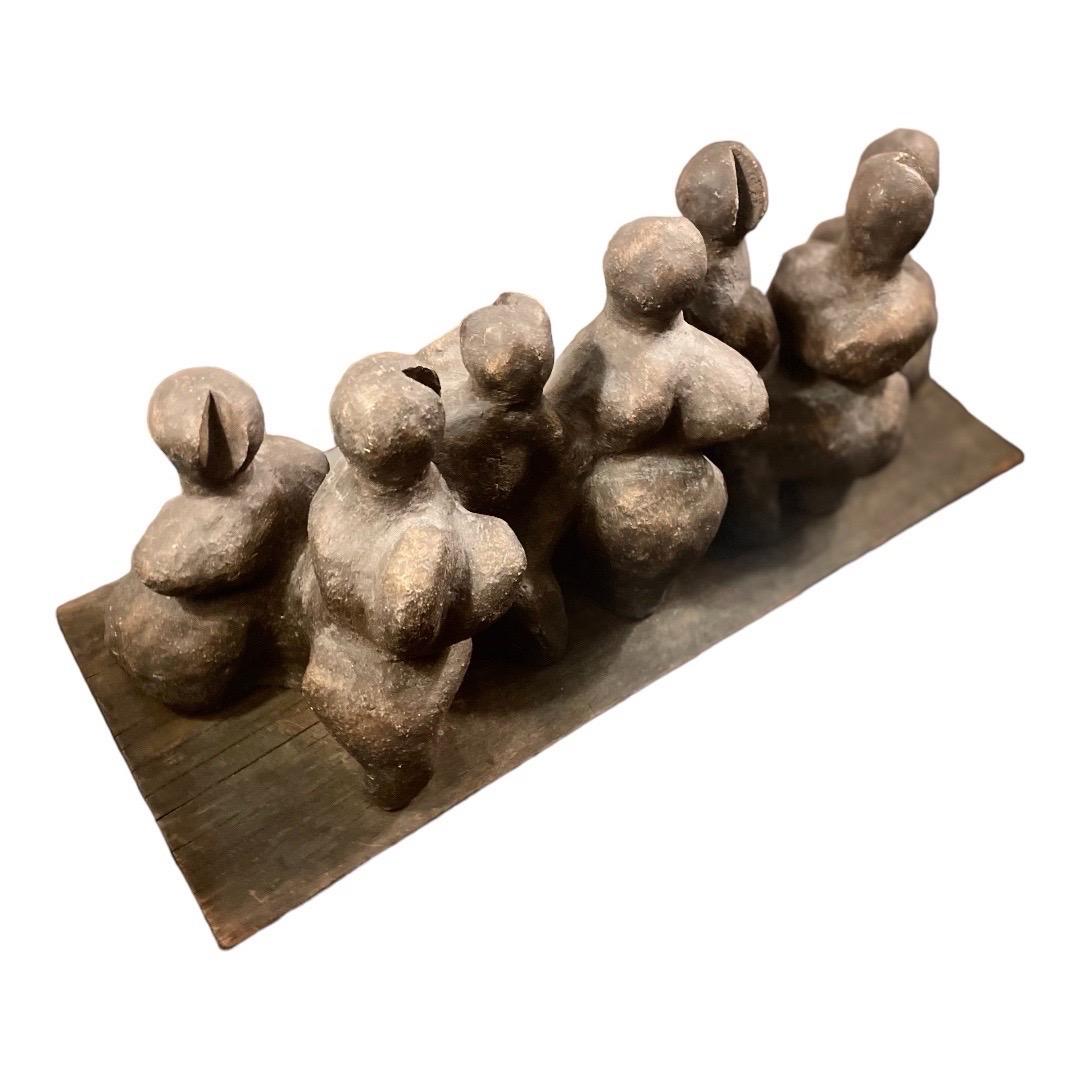 This is a very vintage, marginally figural clay sculpture, depicting what seems to be a group of curvy female characters. 

The unknown artist attached the sculpture to a piece of weathered wood. 

There are no defined facial features, though some