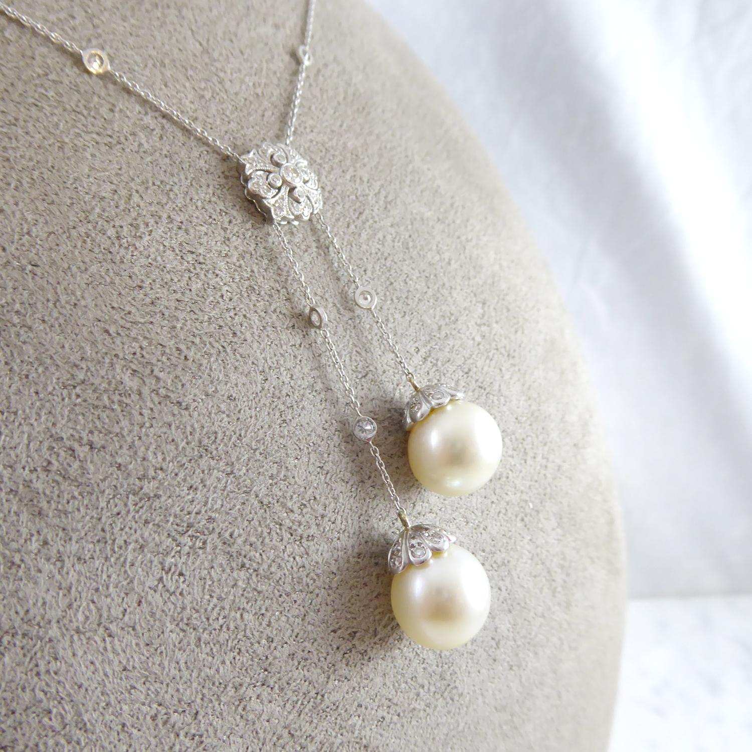 A modern cultured pearl and diamond necklace designed as a central open scrollwork panel, set throughout with 22 diamonds to include a principal round brilliant cut diamond measuring approx. 2.40mm diameter, surrounded by 21 single cut diamonds