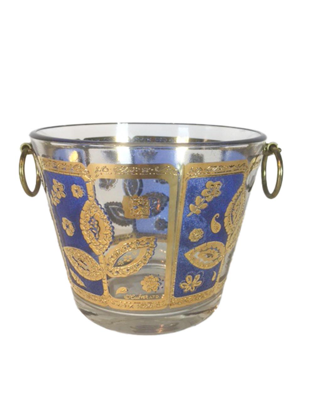 Seven piece barware set consisting of 6 double old fashioned glasses and an ice bowl with ring handles. Clear glass with translucent blue enamel in alternating panels and decorated with leafstems and flowers in raised 22-karat gold. The ice bucket