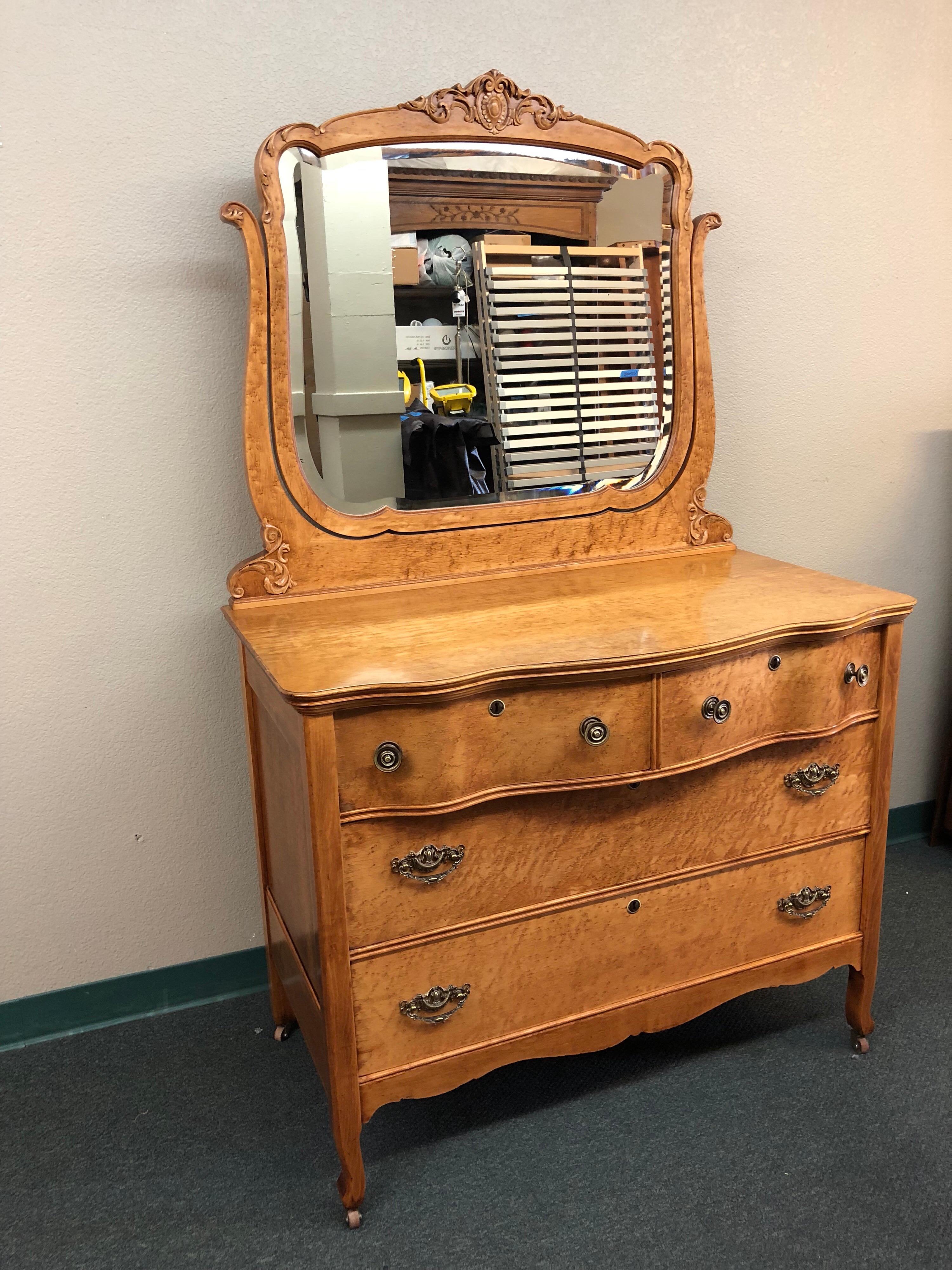 A vintage dresser with mirror. The curly maple woodgrain is only the first of many vintage delights that include curved front drawers, carved flourishes and antiqued brass fittings.
 