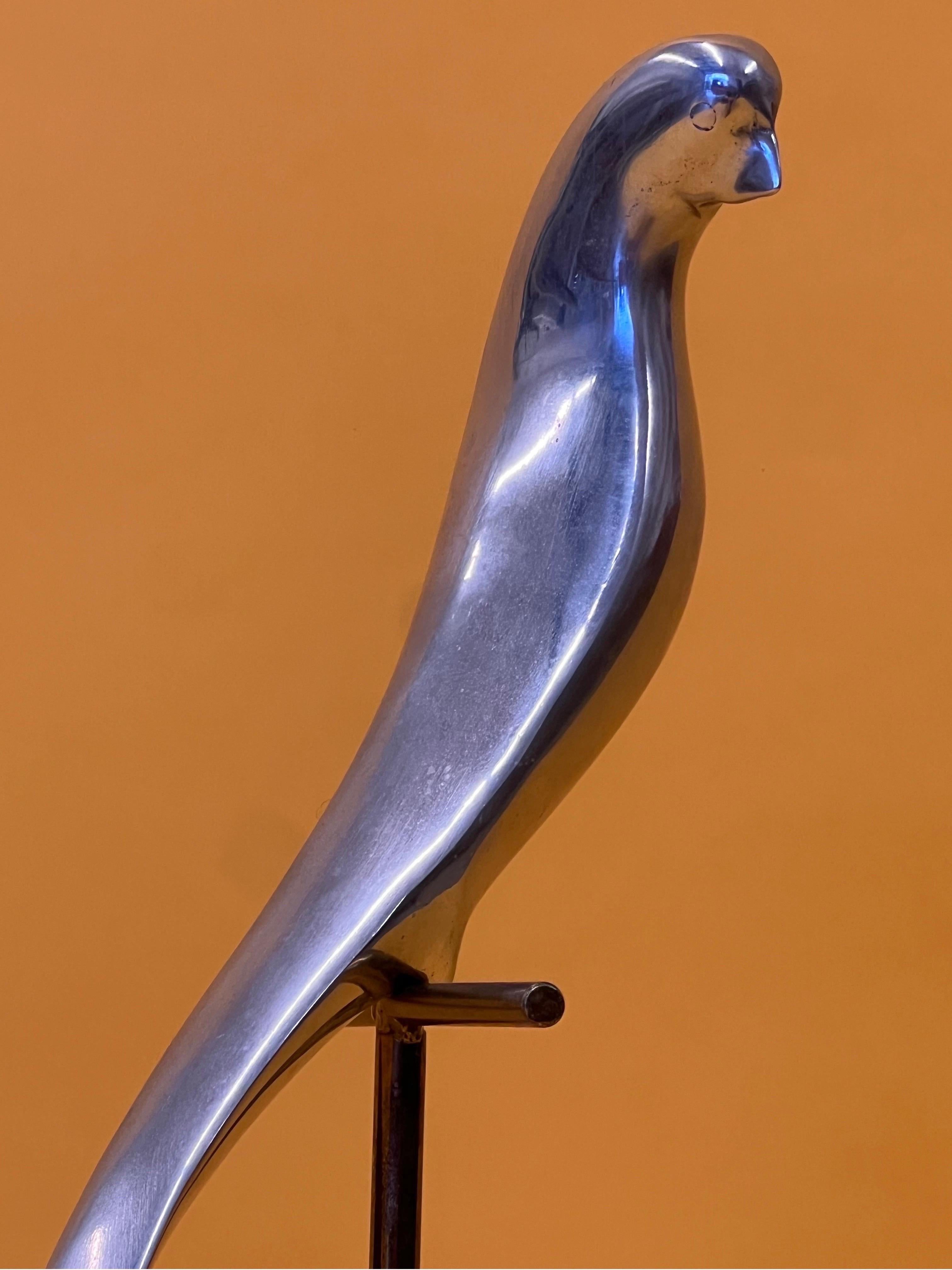 Sculpture des années 1980 réalisée par C.I.C. avec une légère signature encore présente. Un perroquet en aluminium est assis sur un perchoir doré. La base carrée est en marbre avec une plaque dorée. Le perchoir avec perroquet pivote pour permettre