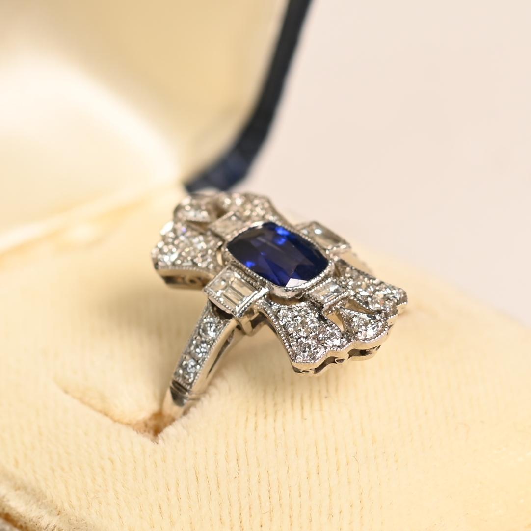 Questo squisito anello con zaffiro taglio cuscino da 1,15 carati è una vera e propria testimonianza di artigianalità ed eleganza senza tempo. La pietra centrale, uno zaffiro naturale dal taglio a cuscino allungato, vanta un'ipnotica saturazione blu