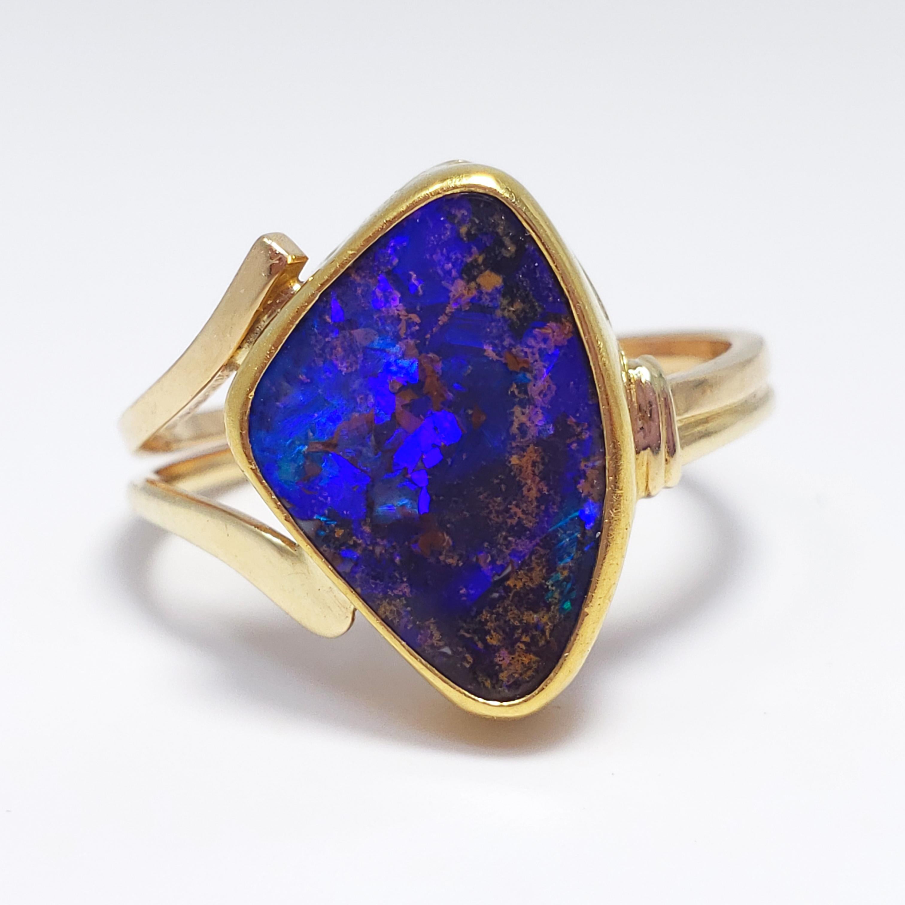 A gorgeous opal in a unique cut! This statement cocktail ring features a custom-cut boulder opal with a mesmerizing, blue, black, and purple play of color in the body. Set in a decorative 22K bezel, connected with a 14K double band which separates