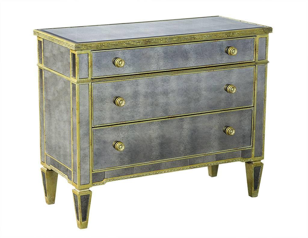 This modern chest is covered in antique mirror panels with a beveled mirror on the top surface.  It has gold finished metal trim on all edges and on the round drawer knobs.  The tapered feet are also covered in mirror and gold metal, making this the