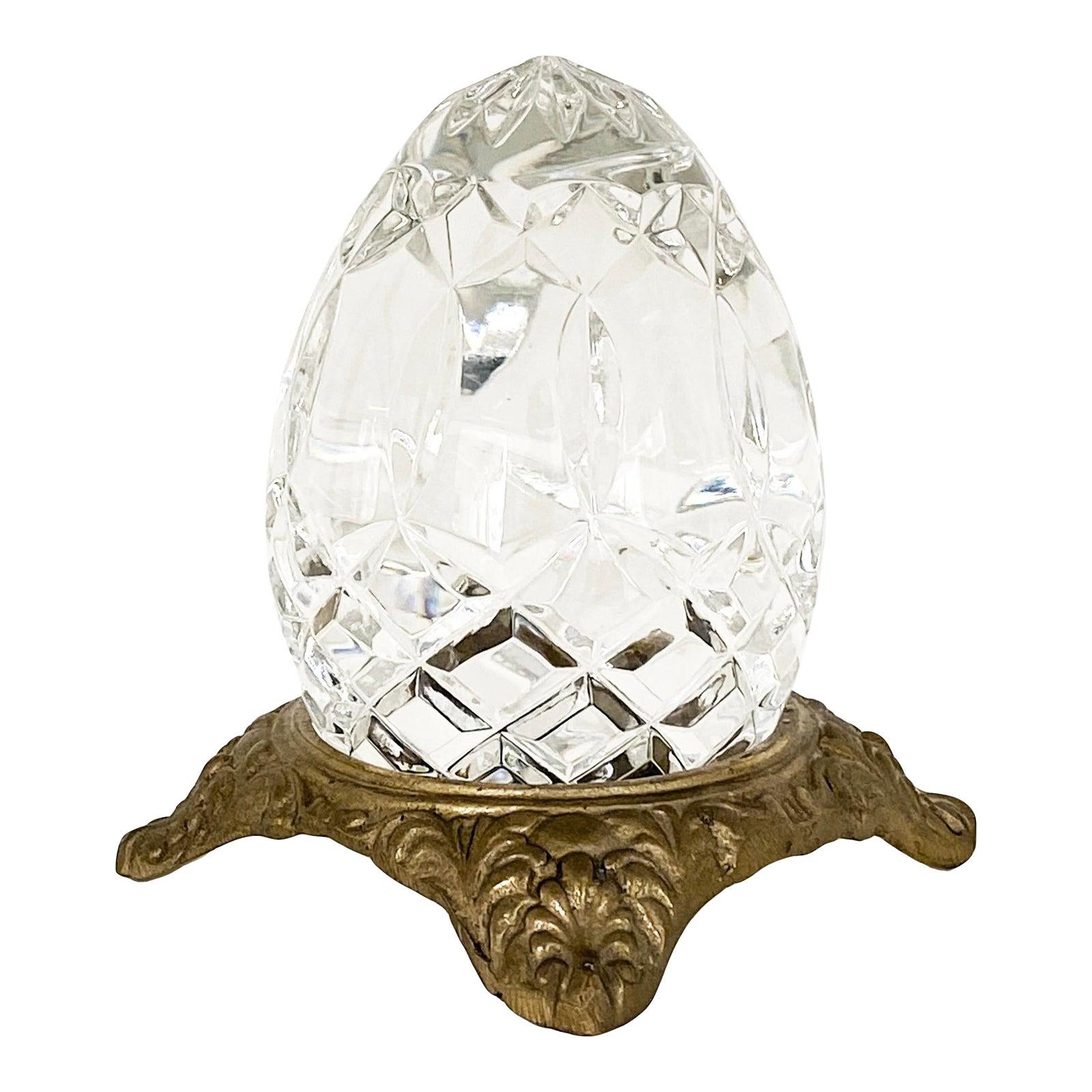 A beautiful crystal glass cut egg-shaped paperweight or decorative item, sitting in a gilt-finished brass stand with ornate detailing. Piece is vintage but in wonderful condition. No scratches or damage to glass.