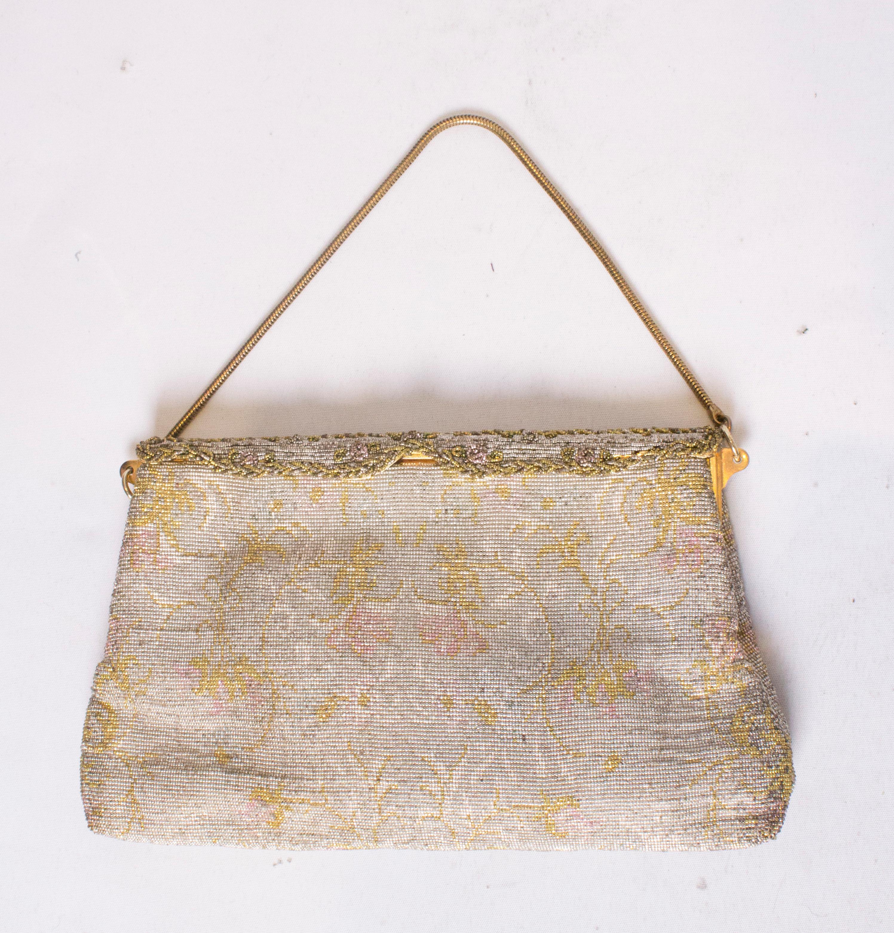 A stunning vintage evening bag is cut steel. The bag has a shaped fold over front, and is lined in satin with two pouch pockets. It has a silver /grey  background with a  pink and yellow  design. Measurements: width 9 1/2'', height 6''.