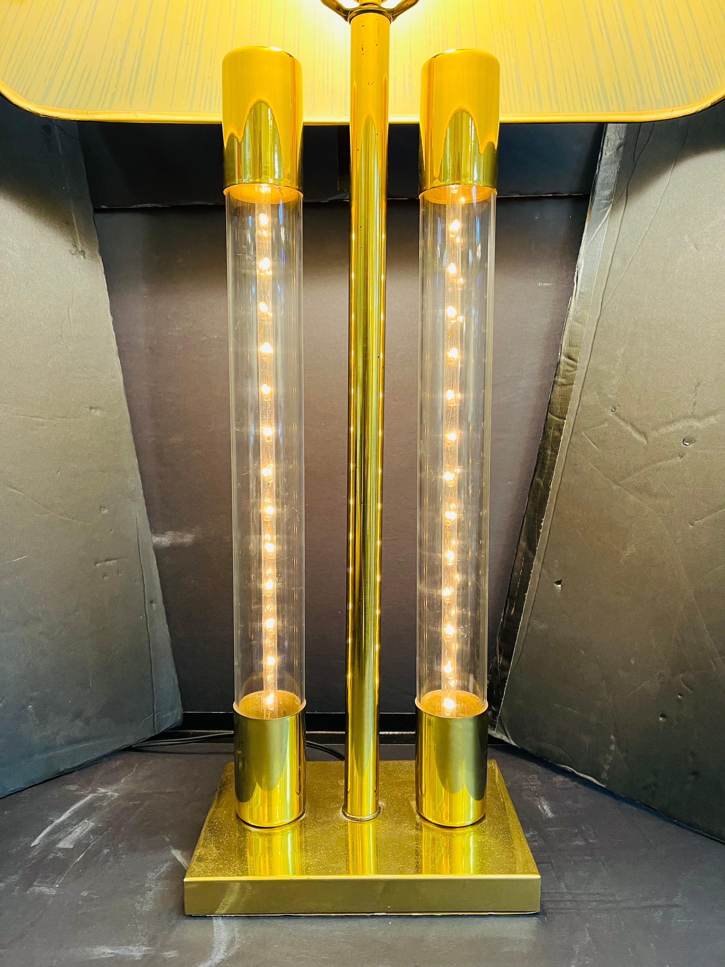 A vintage, late 20th century, brassy and clear tube light up table lamp. The table lamp features a three way switch which allows the light bulb to be illuminated, or the two clear plastic tubes with interior strings of lights to be illuminated, or