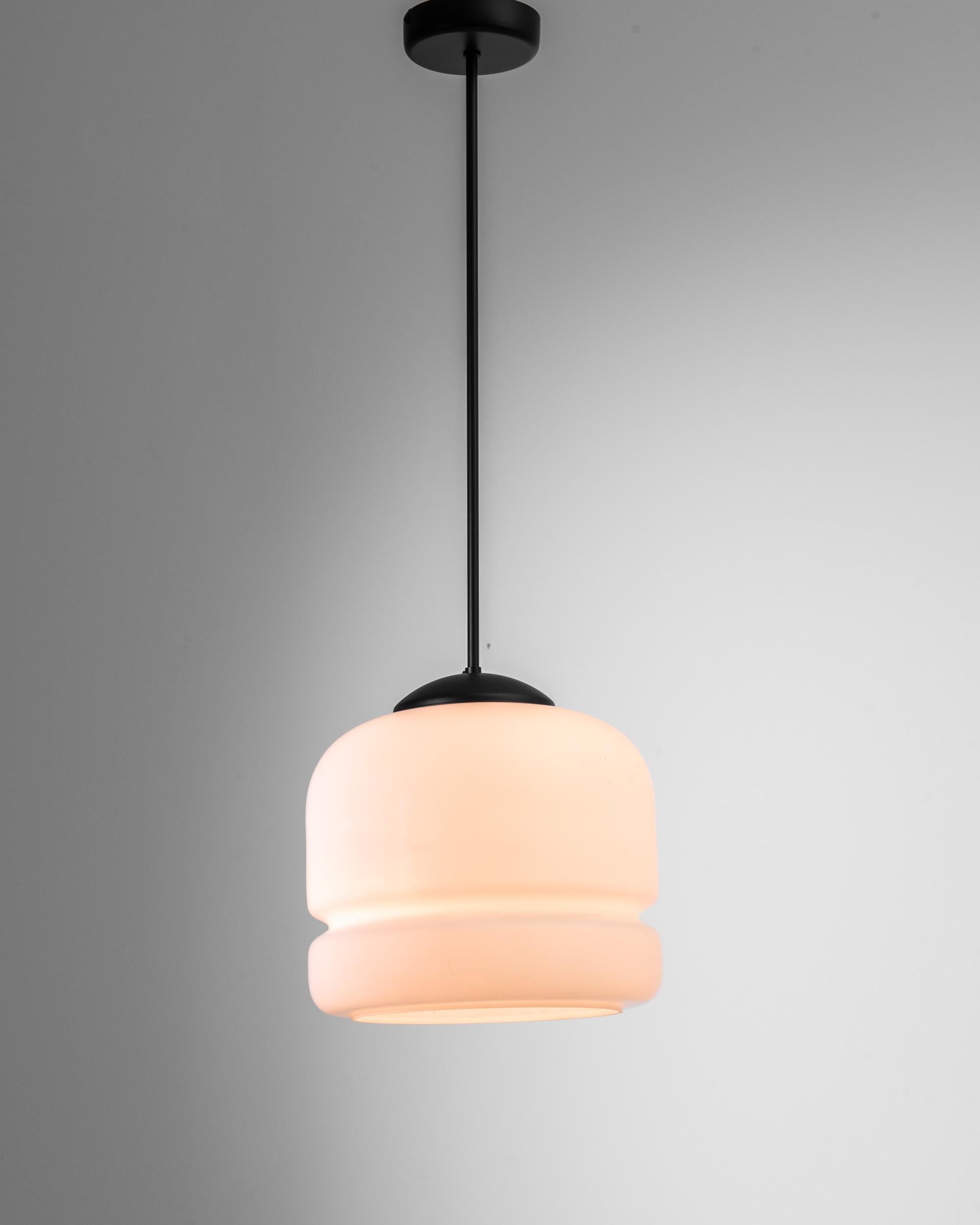 A glass and metal pendant lamp from Czechia, produced during the 20th Century. Descending from the ceiling upon a three foot rod, this charming lamp, with its bulbous, organically curved body of opal glass, feels constantly contemporary. Like two