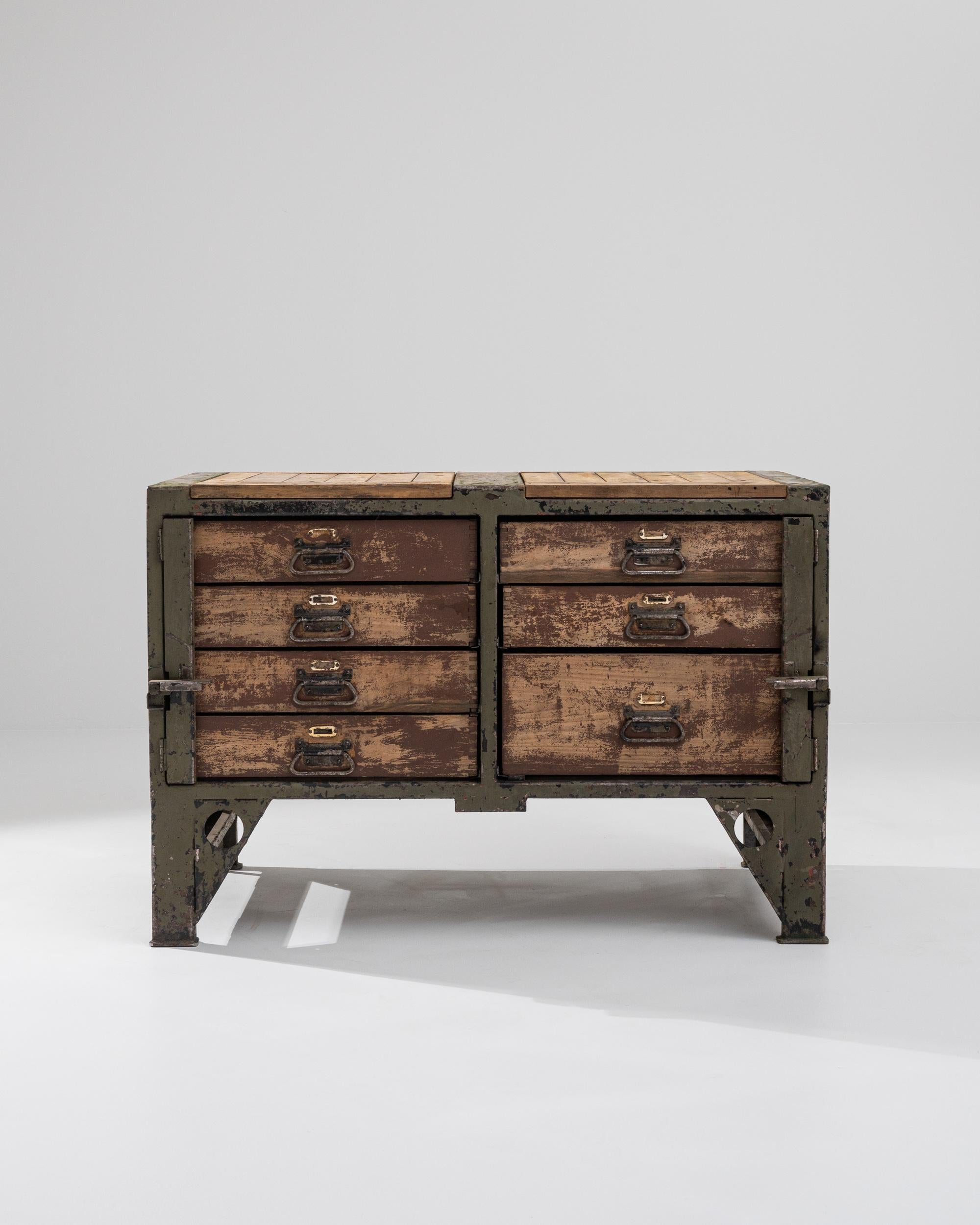 A metal and wooden chest of drawers from 20th century central Europe. Matured, yet compellingly spry, this industrious set of drawers radiates a charming and tidy sensibility. Composed of seven sliding drawers underneath its time-worn work surface,