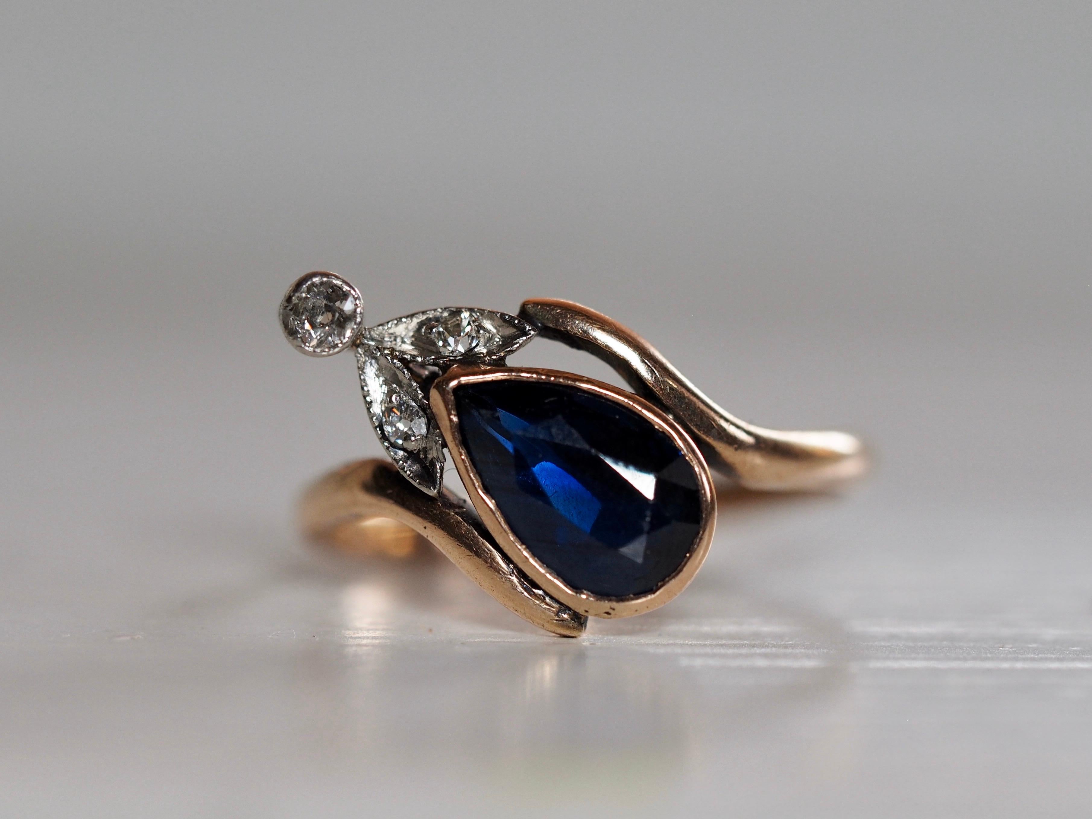 This elegant Art Deco ring holds a stunning 1.58 carat blue sapphire pear shaped center, bezel set in 14- karat yellow gold. The center is accented with a delicate touch of three old minor and old European cut diamonds set above the sapphire in a