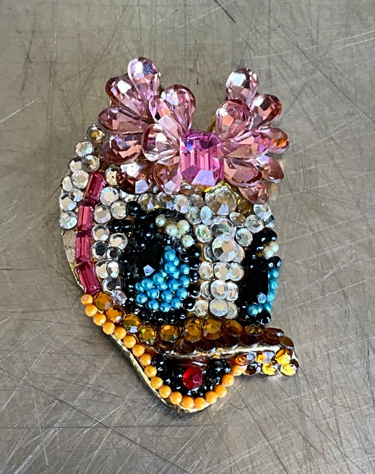Este broche forma parte de una colección de pins de personajes Disney diseñados por Wendy Gell a finales de la década de 1980, muy codiciados por los coleccionistas. Piezas como los broches del Pato Donald y Daisy, con cuentas, cristales y