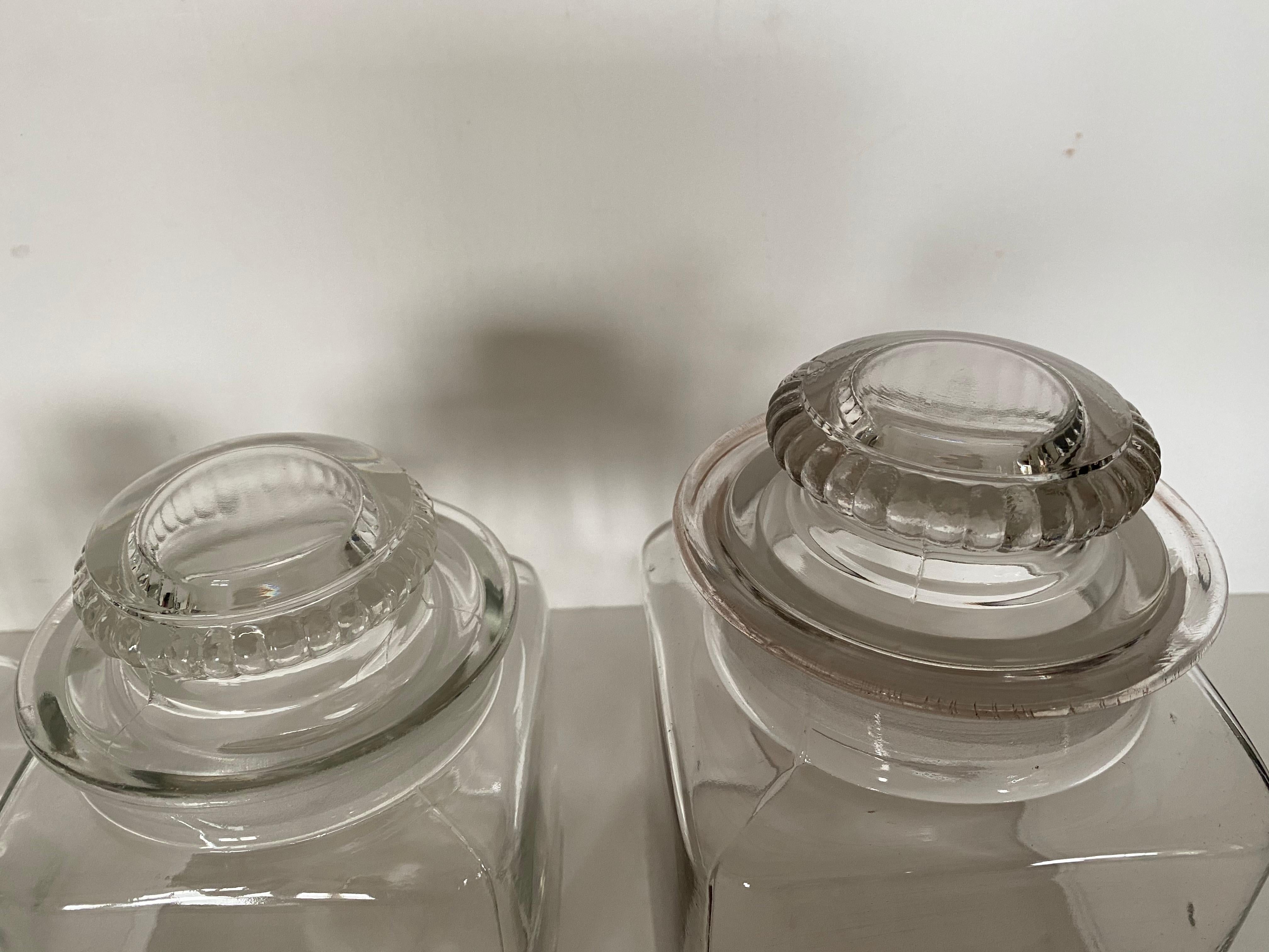 Set of 4 1920s Dakota graduated size square clear glass pharmacy canister jars with ground glass lid stopper. These glass canisters are wonderful to be displayed in the open to hold your favorite food items, pet food, treats! They are air tight so
