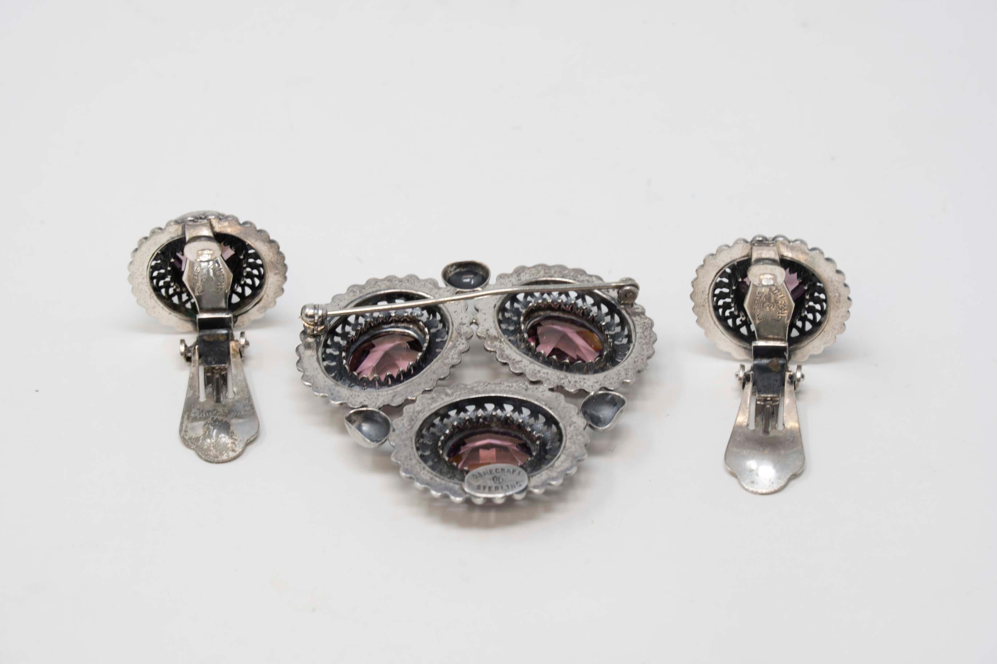 Vintage art deco style Danecraft sterling silver set of brooch and clip-on earrings with amethyst glass stones. Made in USA circa 1950-60. Stamped on the back, brooch measures 38mm long x 45mm wide. Each earring measures 25mm x 20mm. In good