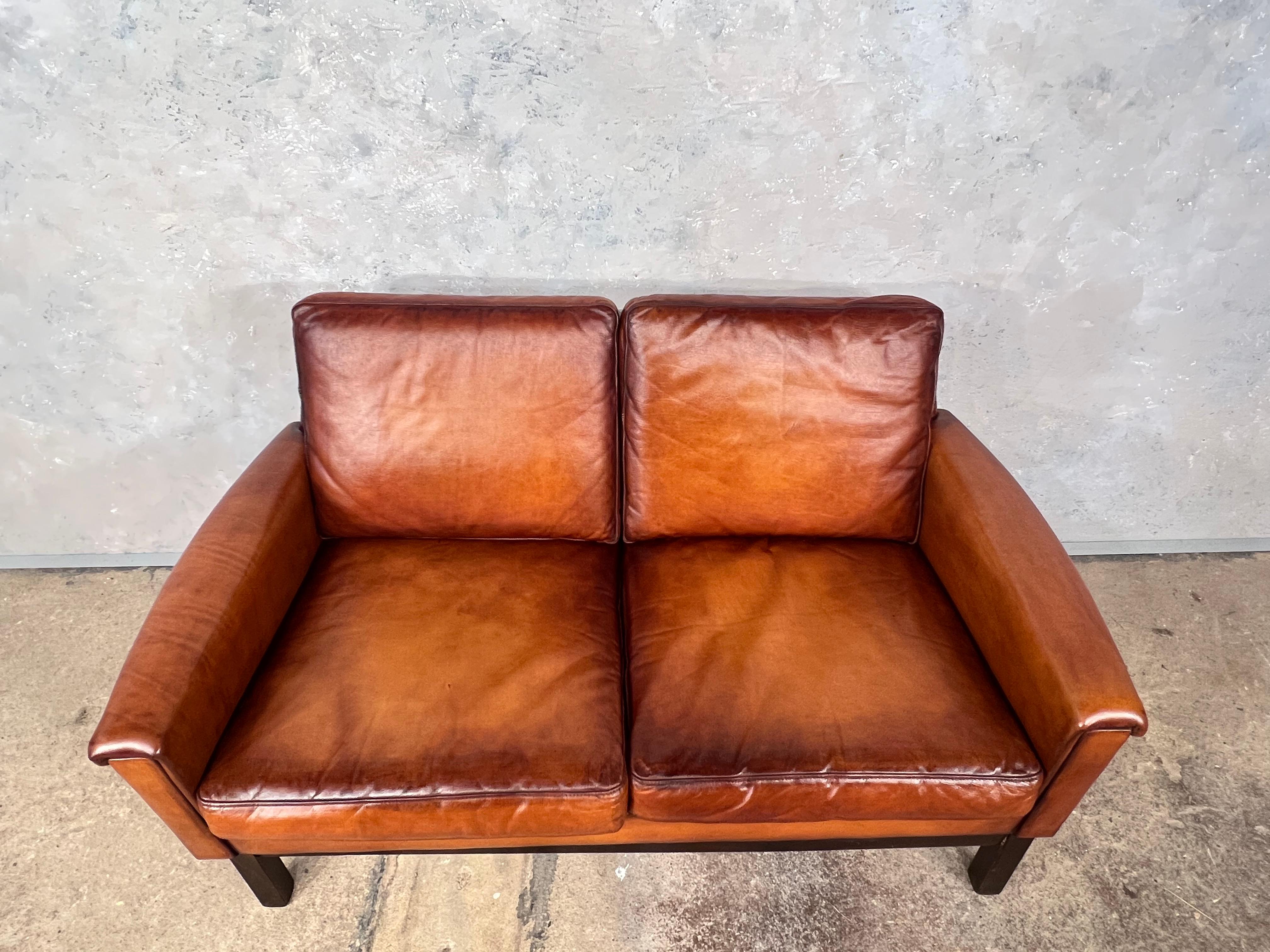 Vintage Danish 70s mid-century tan twoseater leather sofa.

Very stylish with a beautiful shape, compact size but still comfortable, great design, resting on a solid Beech plinth, in great vintage condition, restored and hand dyed a beautiful tan