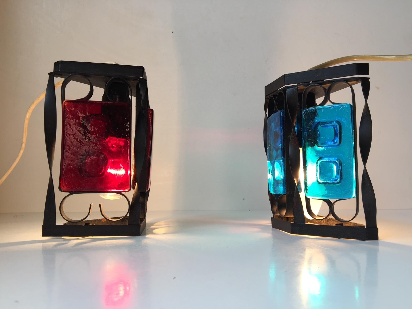 A set of Danish black iron and colored glass sconces. Manufactured and designed in the 1970s as a collaboration between Dantofte and Holmegaard. Measurements: H 16/14 cm (6.2/5.8 inch), W 12/13 (4.8/5.2 inch). Similar to designs by Claus Bolby and