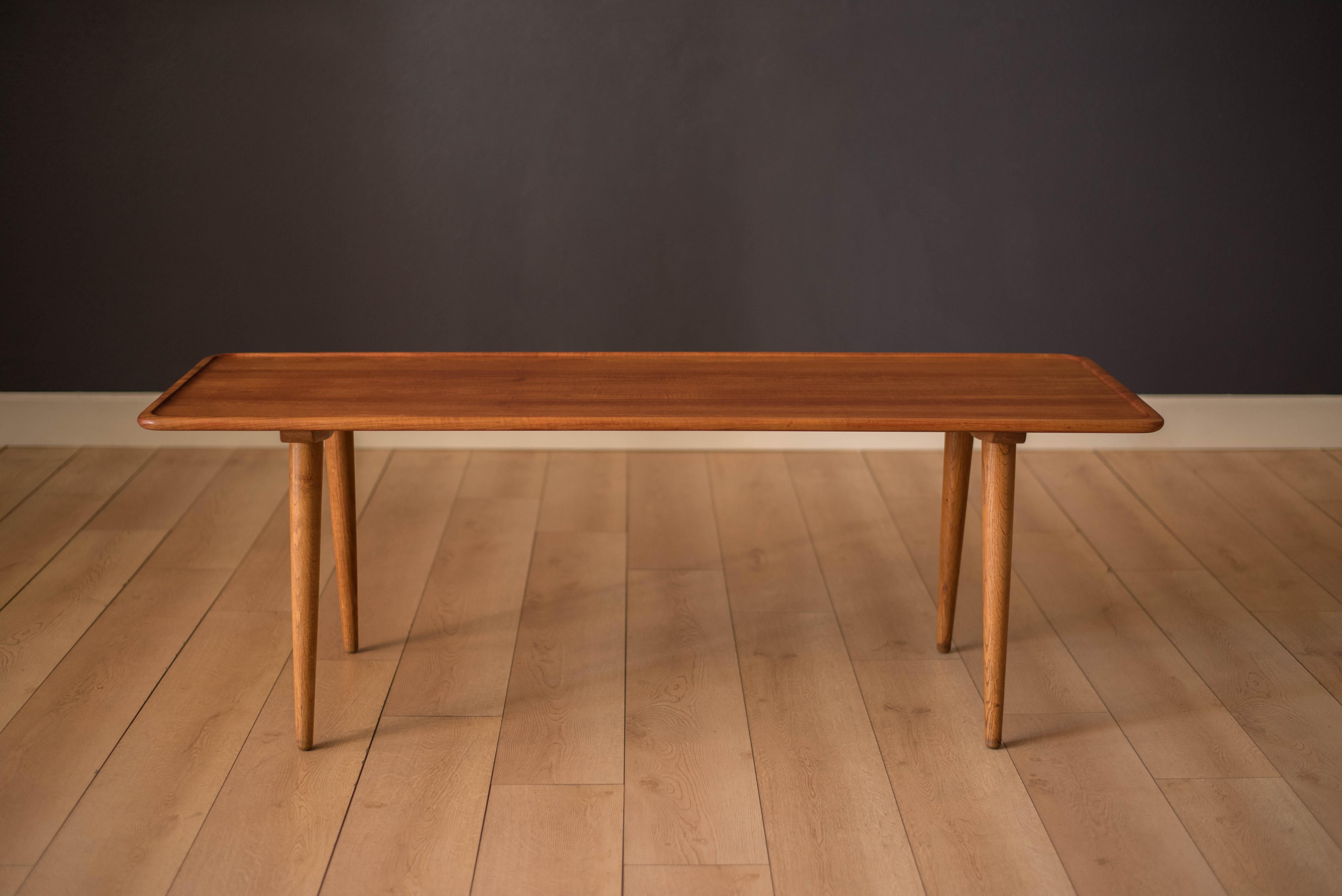 Mid-Century Modern original coffee table designed by Hans Wegner for Andreas Tuck model AT-11. This solid planked teak tabletop displays a sleek Minimalist design with raised rounded edges. Supported by four sturdy oak legs that splay at an angle.