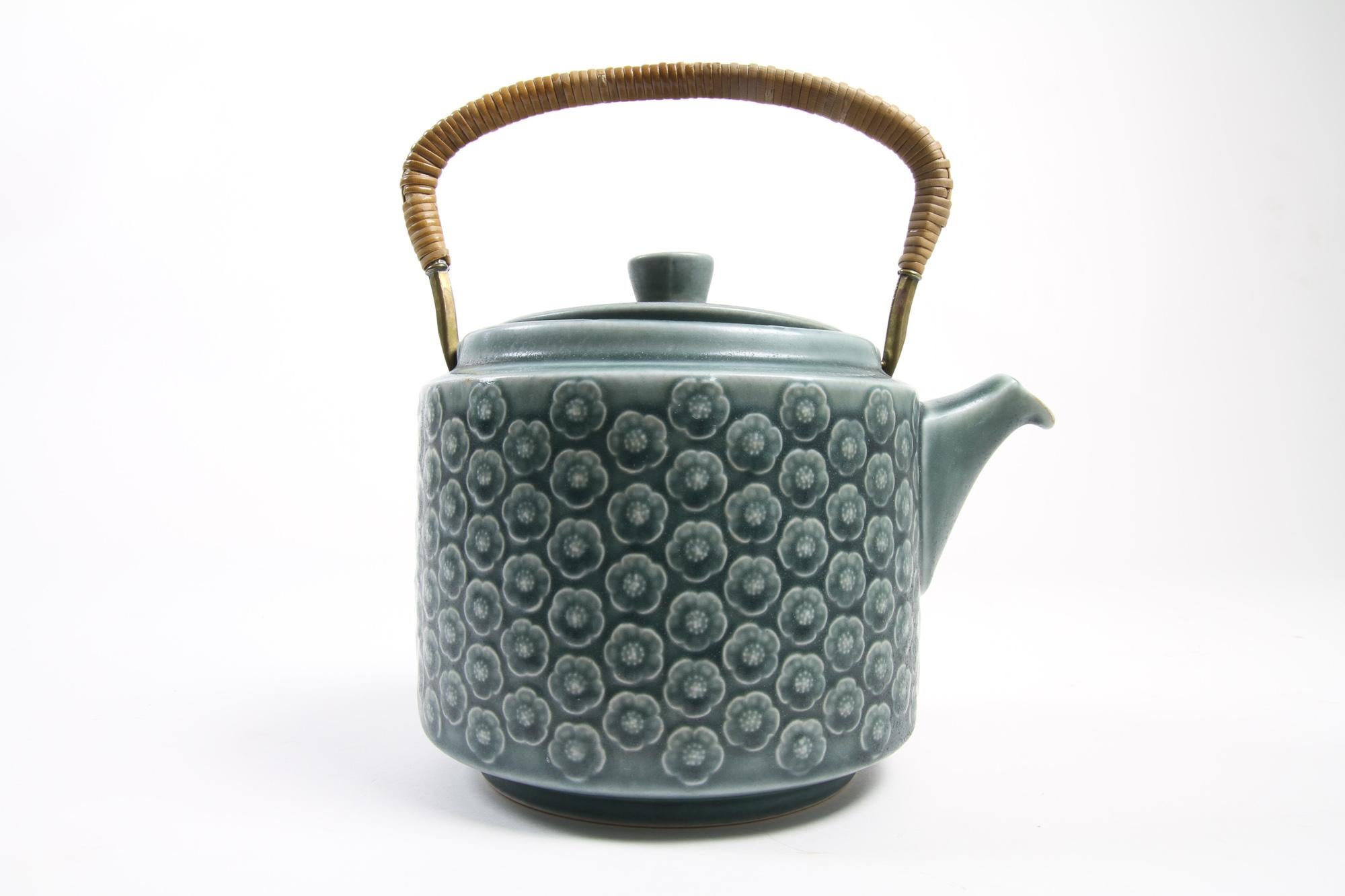 Vintage Danish Azur stoneware teapot by Jens H. Quistgaard for Kronjyden, 1960s.
This beautiful Mid-Century Modern stoneware by IHQ set consists of a tea pot with lid and a small square bowl. Tea pot handle in brass wrapped in cane. Very lovely