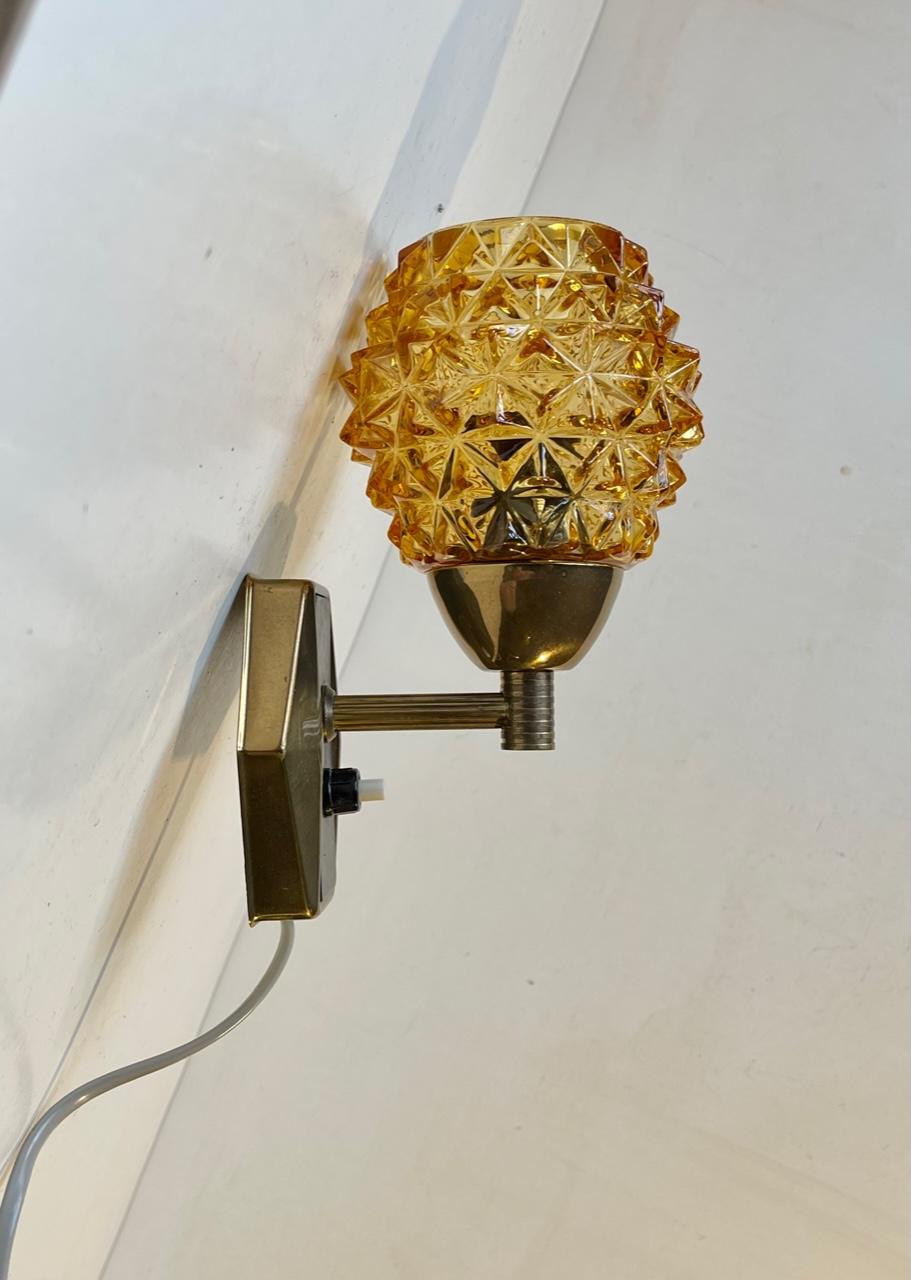 Stylish wall light manufactured and designed by J. Sommer in Denmark during the early 1960s. Its made from partially lacquered brass and has Diamond/pin-apple Patterned amber glass shade. Makers label to the backside of the mount. Measurements: H:
